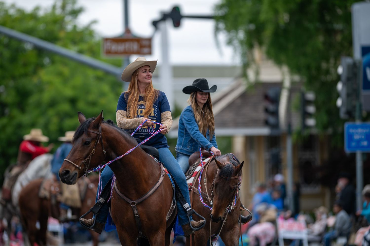 Western-style equestrian riders participating in a community parade along a tree-lined street.