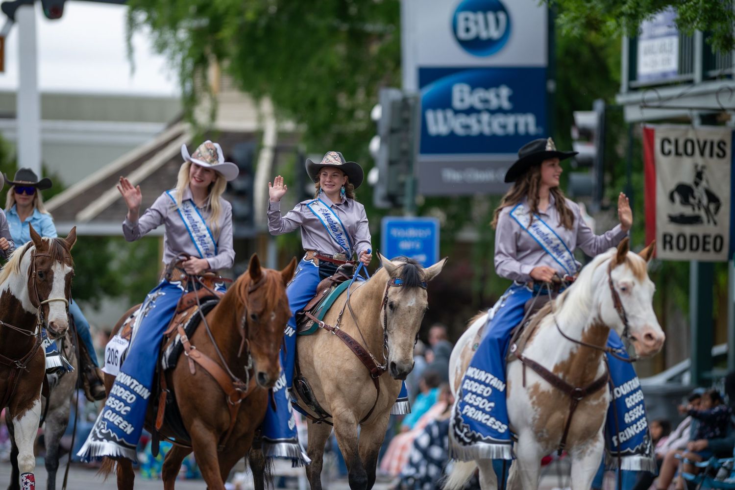 Riders in matching western outfits parade down a street on horseback.