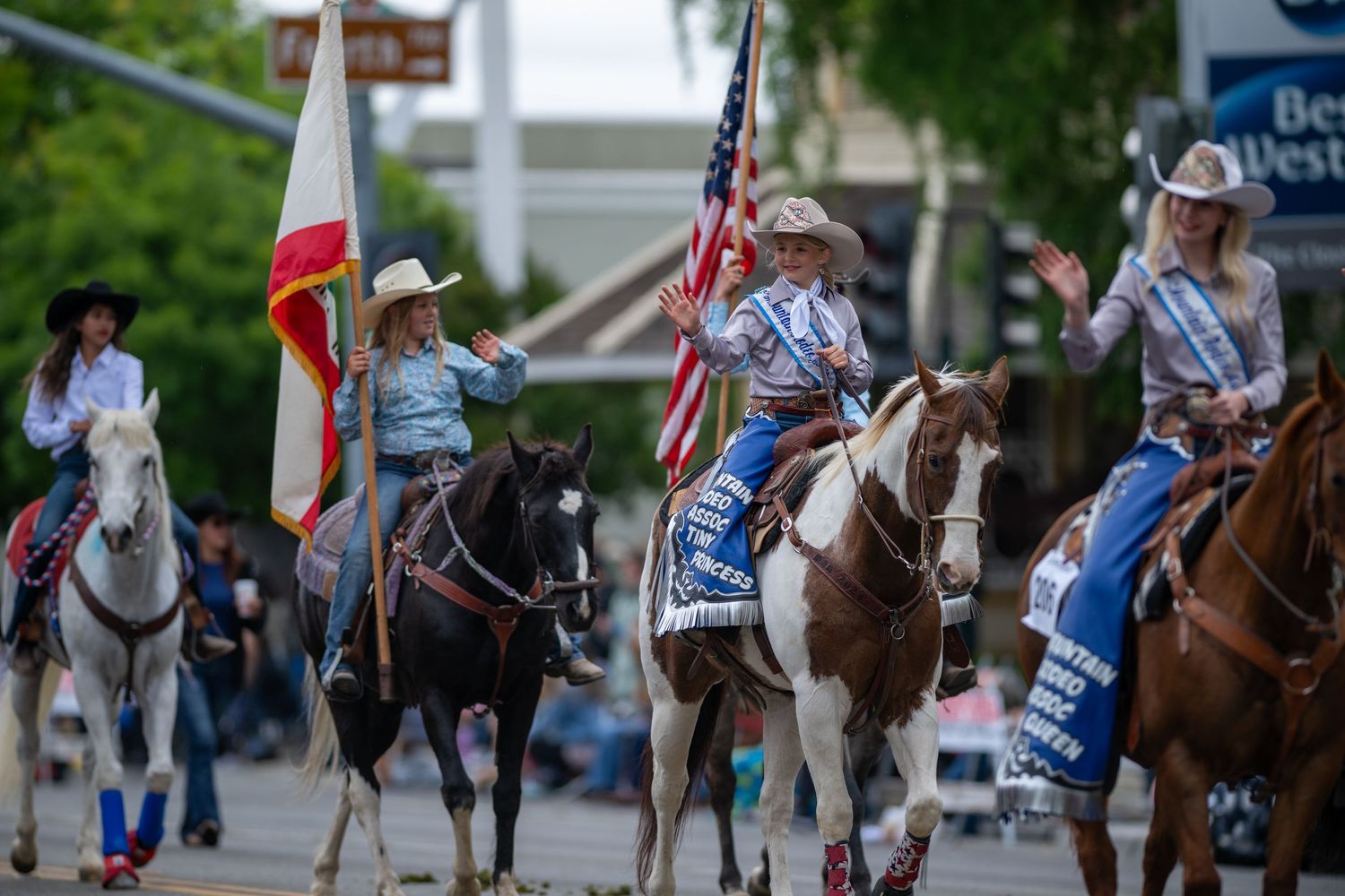 Horseback riders carrying American and other flags proceed down a city street.