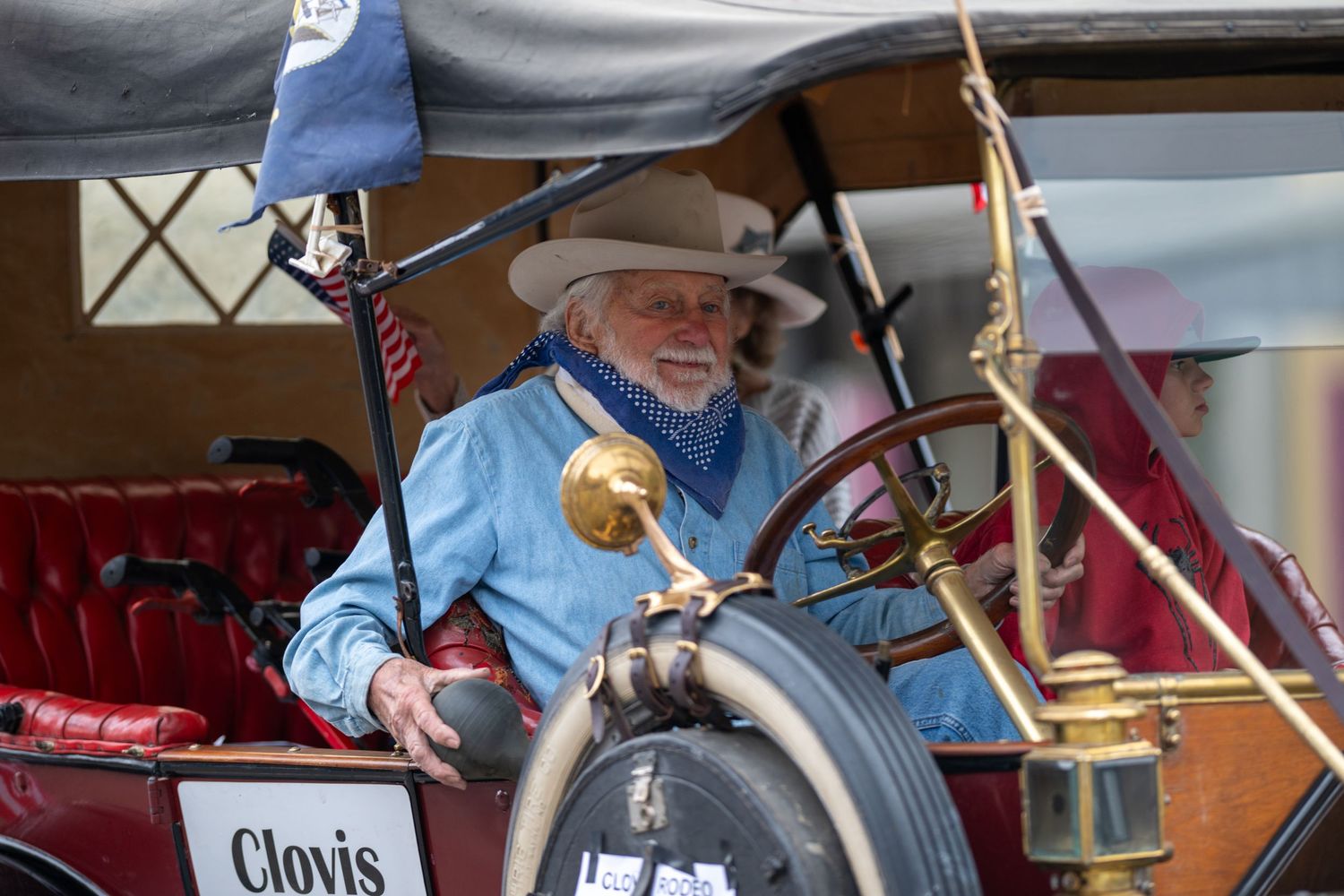 Person driving an antique car in a parade past Best Western hotel.