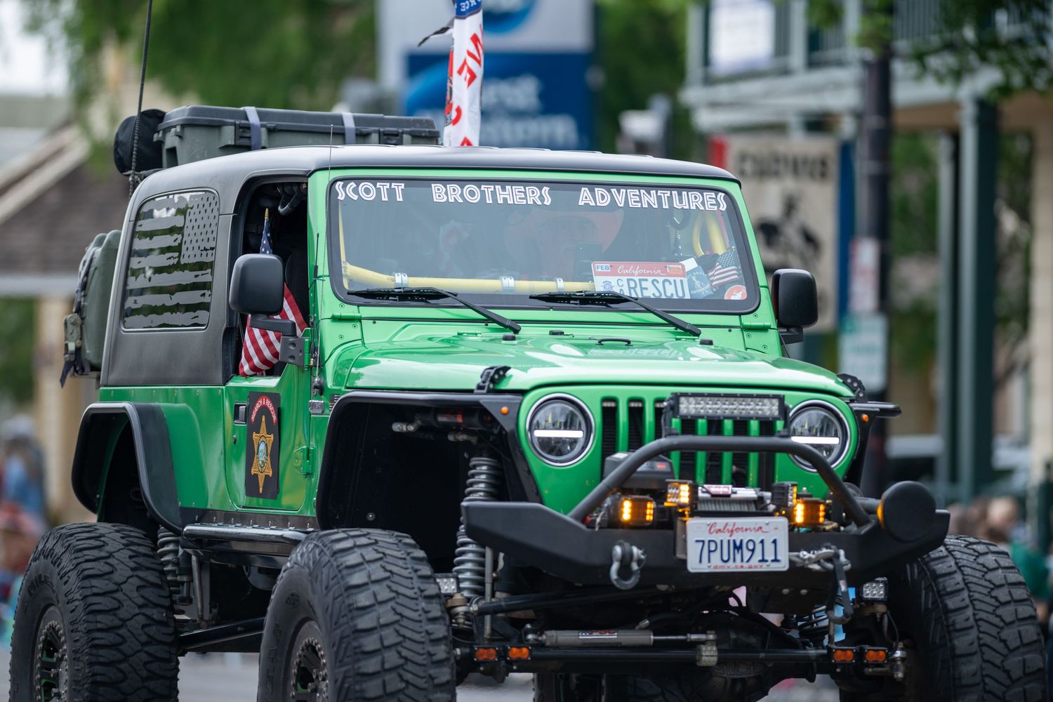A modified bright green Jeep with large off-road tires and custom bumpers displayed at a parade.