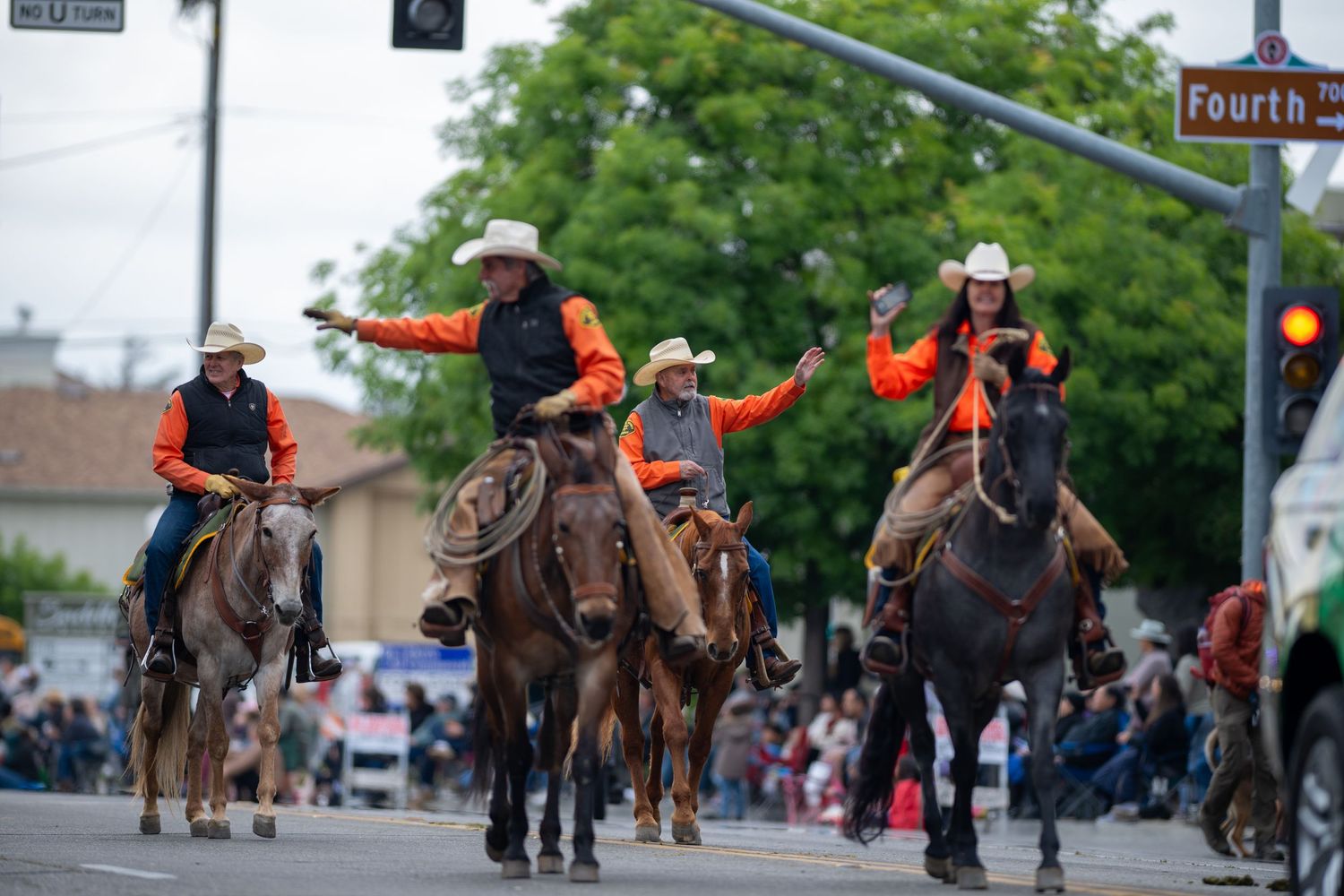 Mounted riders in orange safety vests and cowboy hats participating in a parade procession.