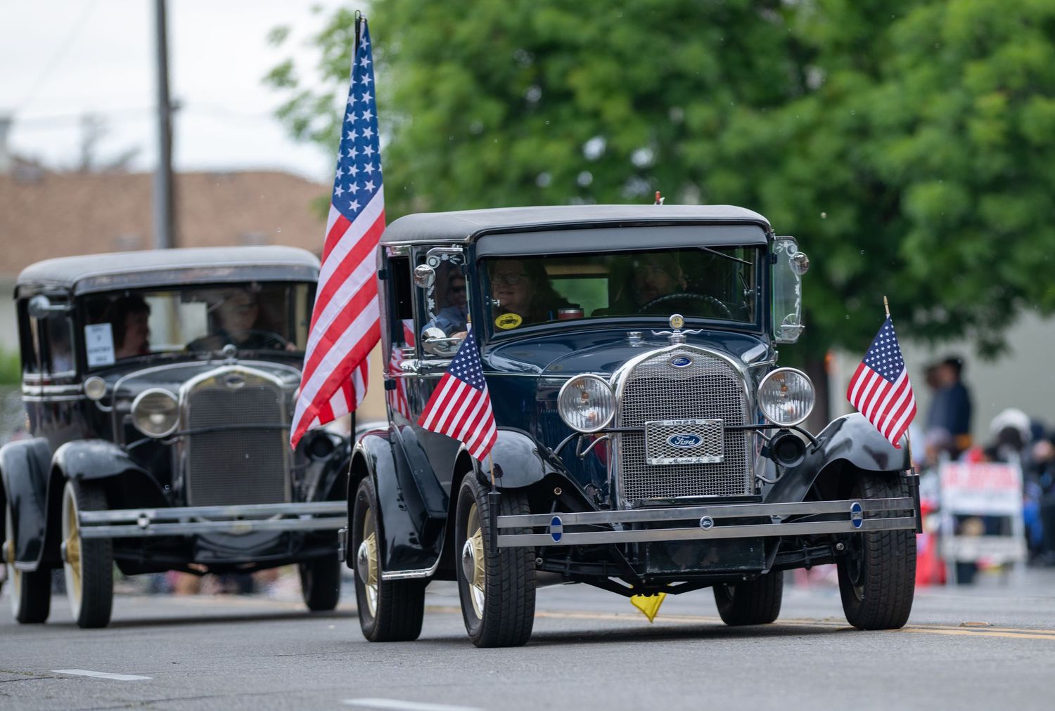 Classic vintage Ford Model A cars decorated with American flags driving in a patriotic parade.