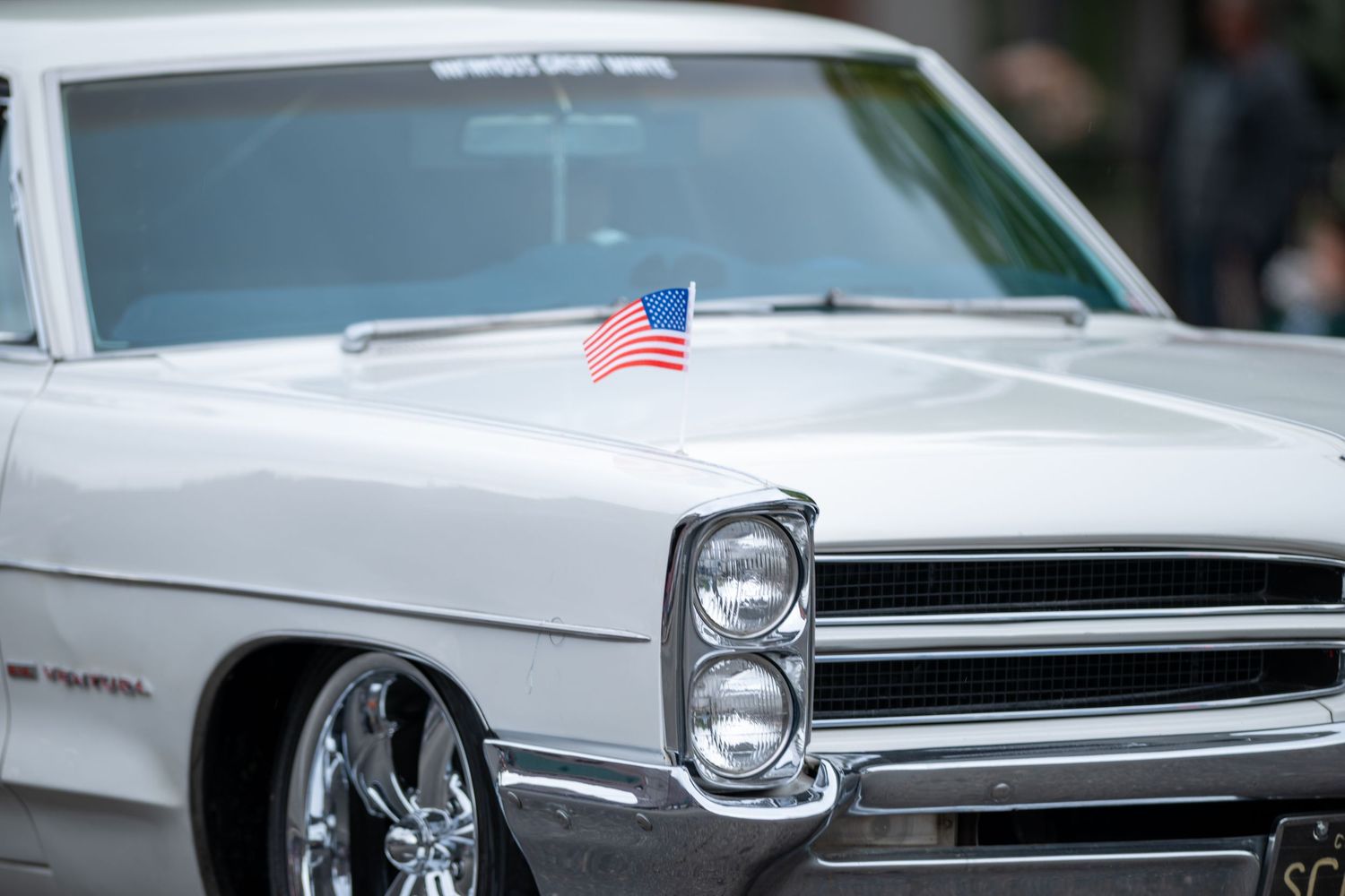 White classic Pontiac with an American flag detail displayed at a parade.