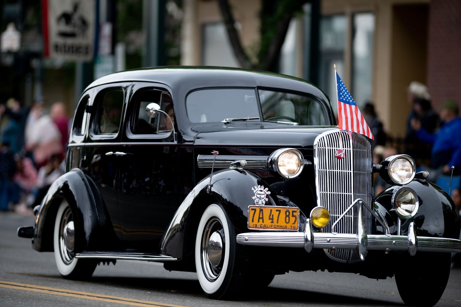 Vintage 1930s Pontiac sedan with American flags participating in a holiday parade.