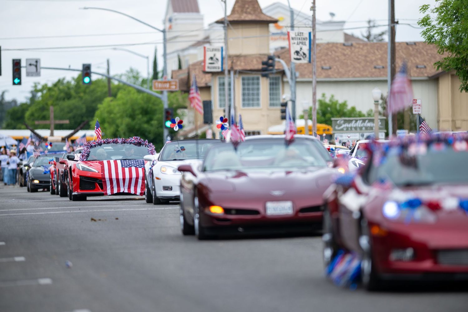 A parade of red cars decorated with American flags drives down a city street.