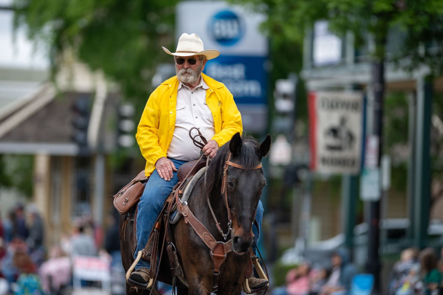 A horseback rider in a yellow jacket rides through a small town street.
