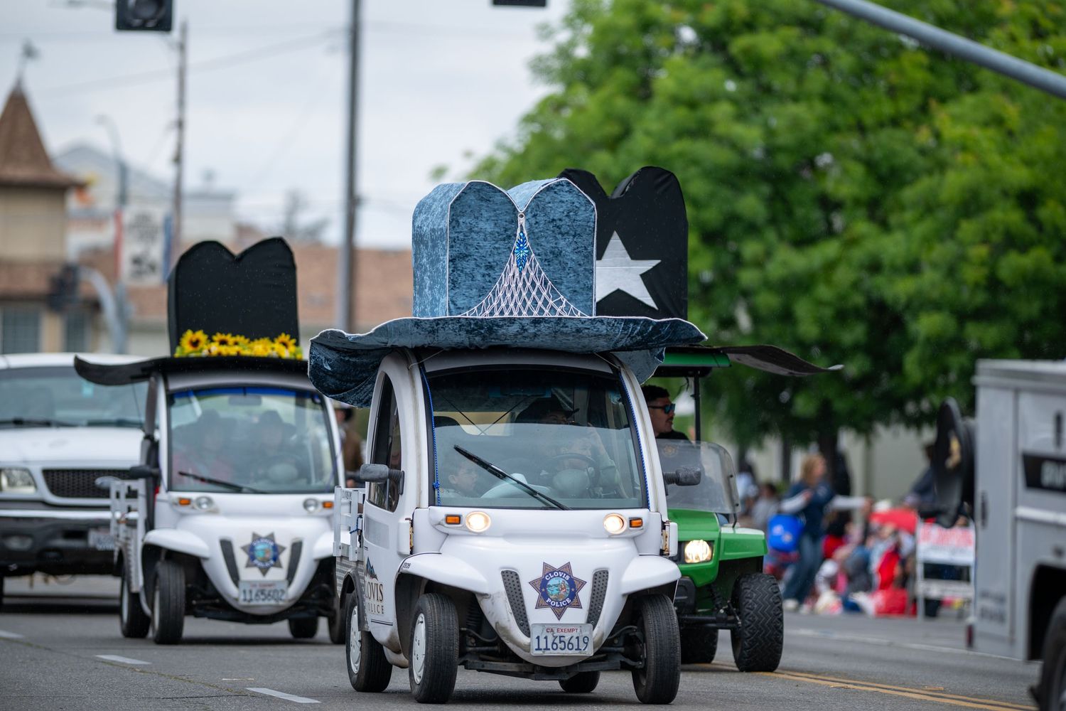 A decorated golf cart with a large cowboy hat on top drives in a parade.
