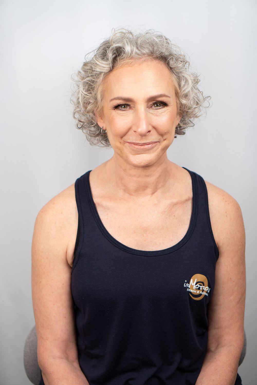 Portrait of a person in a black tank top with curly gray hair against light background.