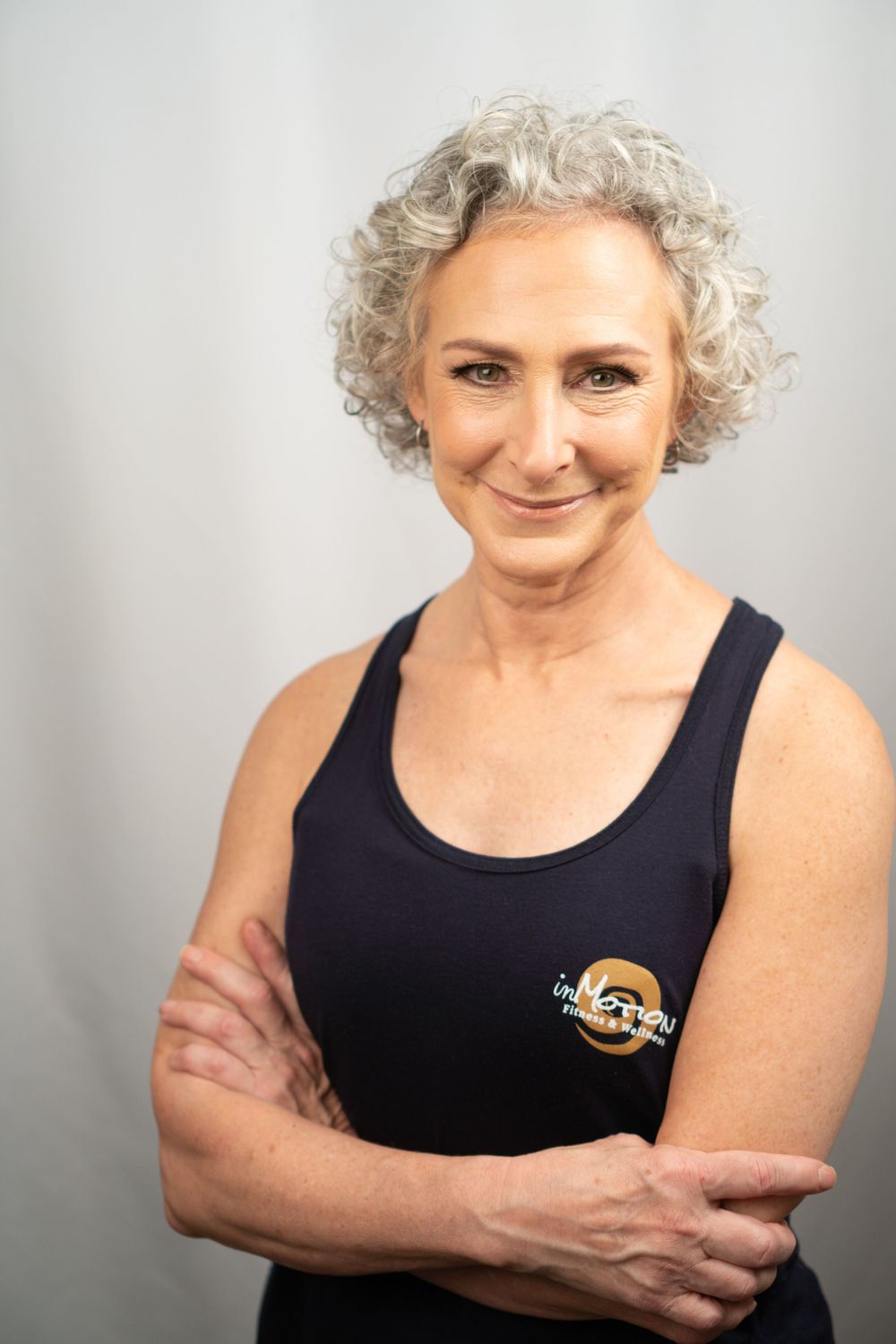 Portrait of a person in athletic wear with silver curly hair against light background.