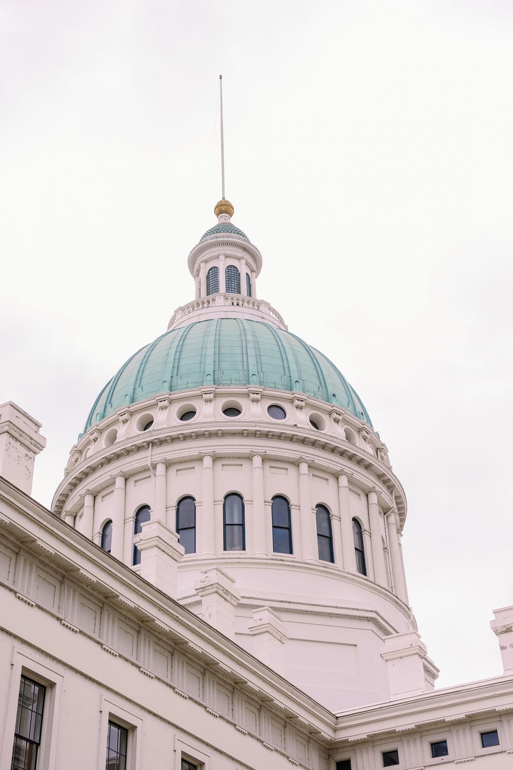 The copper-domed dome of the Old Courthouse building in St. Louis features classical architecture against a cloudy sky.