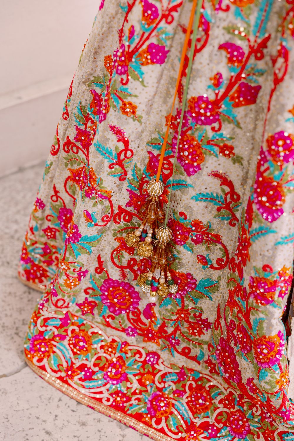 Detailed embroidery on traditional Indian bridal lehenga with pink and red floral patterns and tassels.