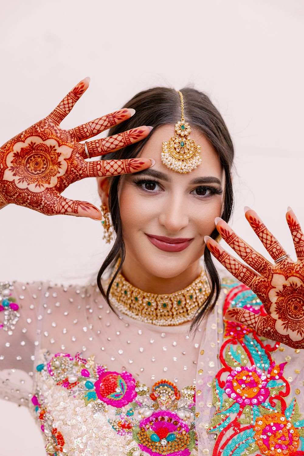 Traditional bridal mehndi design on hands with ornate gold jewelry and colorful embroidered dress.