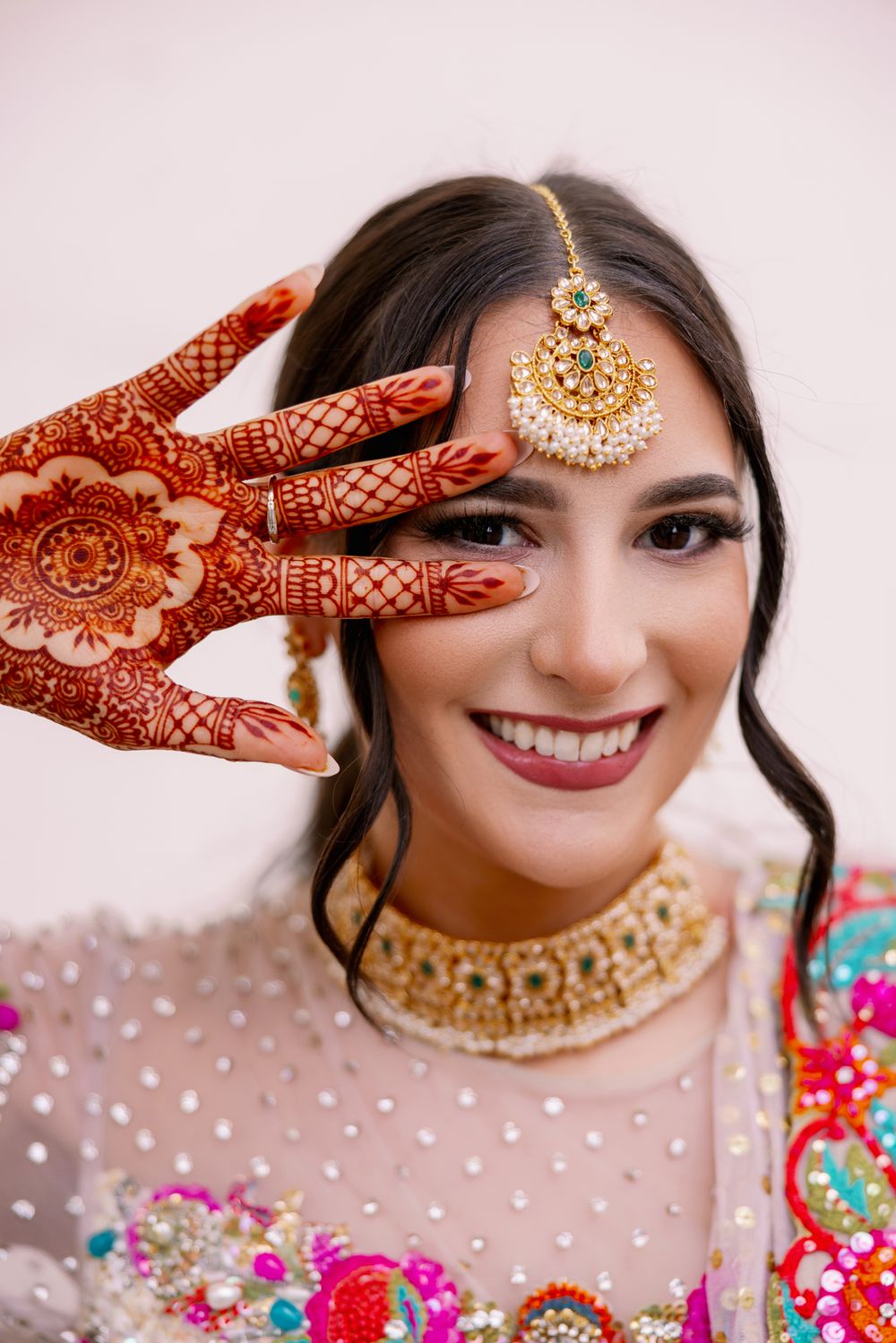 Traditional Indian bridal look showcasing intricate henna design on hand with ornate jewelry and embroidered attire.