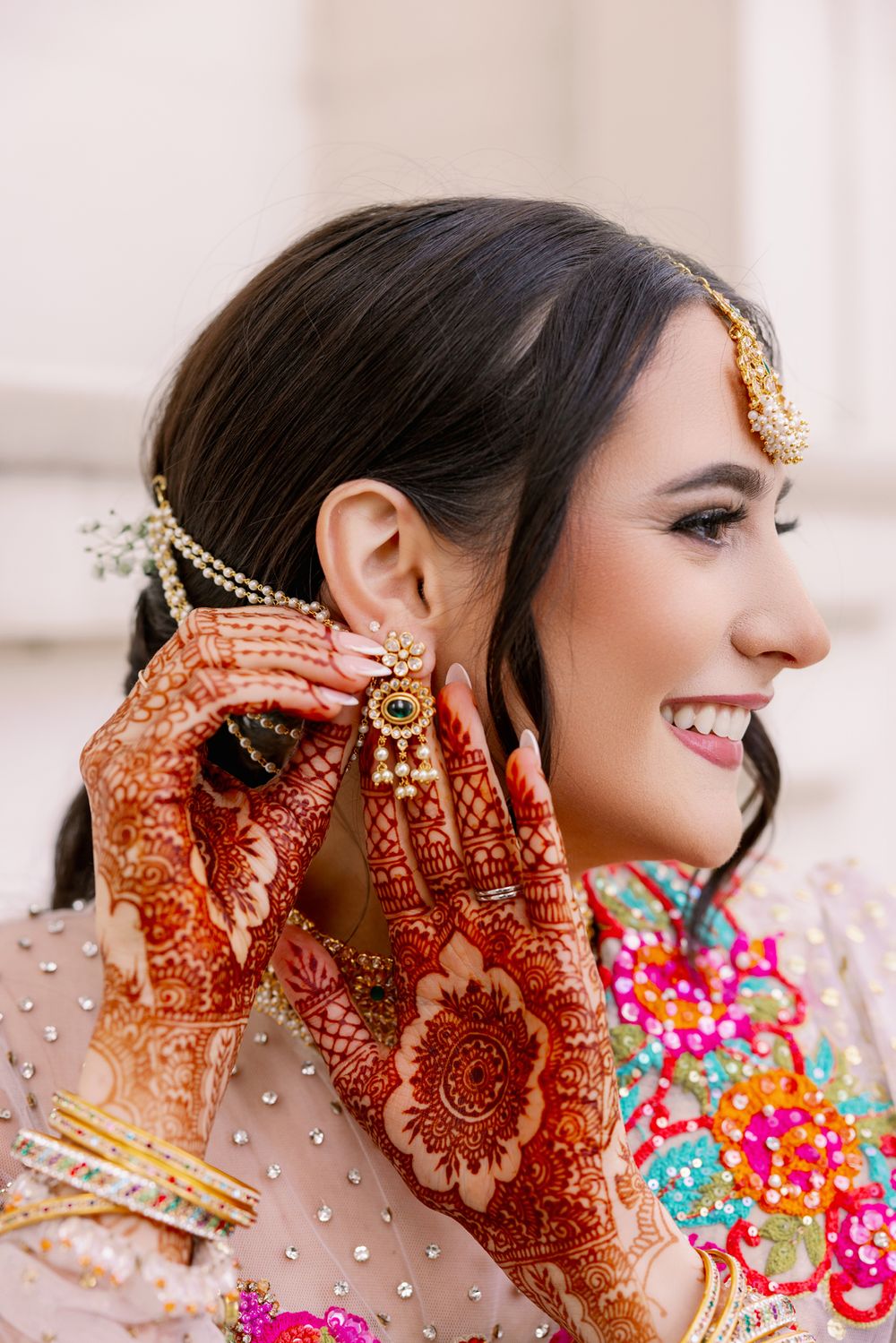 Beautiful traditional bridal portrait showcasing intricate henna designs and colorful floral embroidery details.