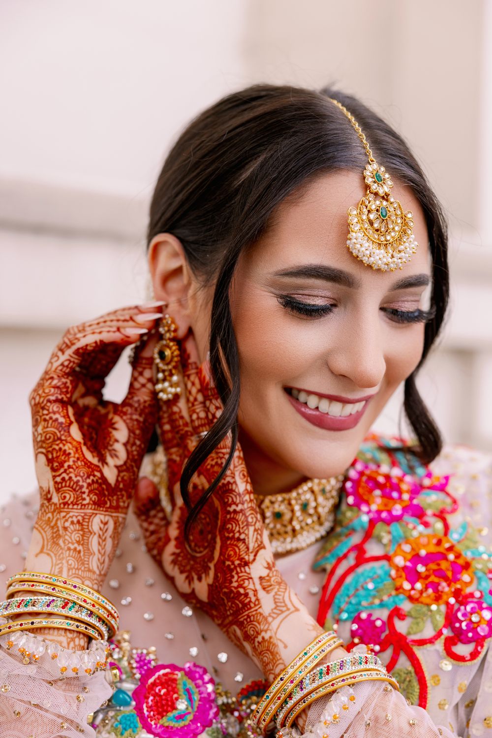 Close-up of South Asian bride wearing gold tikka jewelry and traditional mehndi on hands.