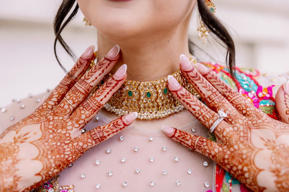 Close-up of intricate henna designs on hands with traditional gold jewelry and embroidered outfit.