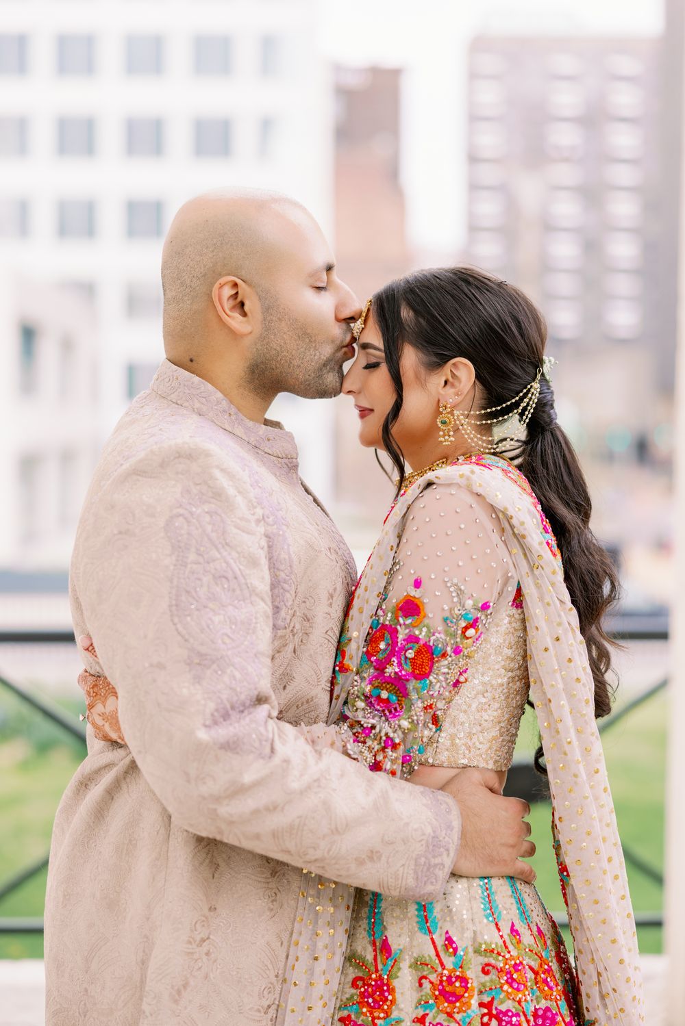Romantic portrait of couple in soft pink traditional outfits against urban backdrop.