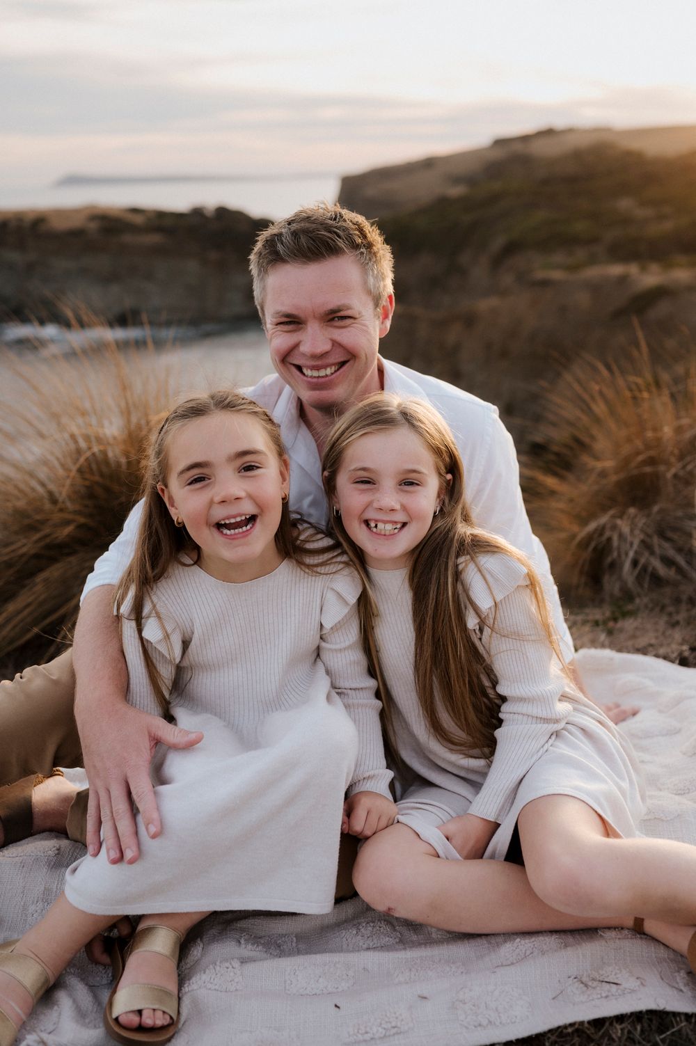 Joyful group portrait on coastal cliff during golden hour wearing matching white outfits.