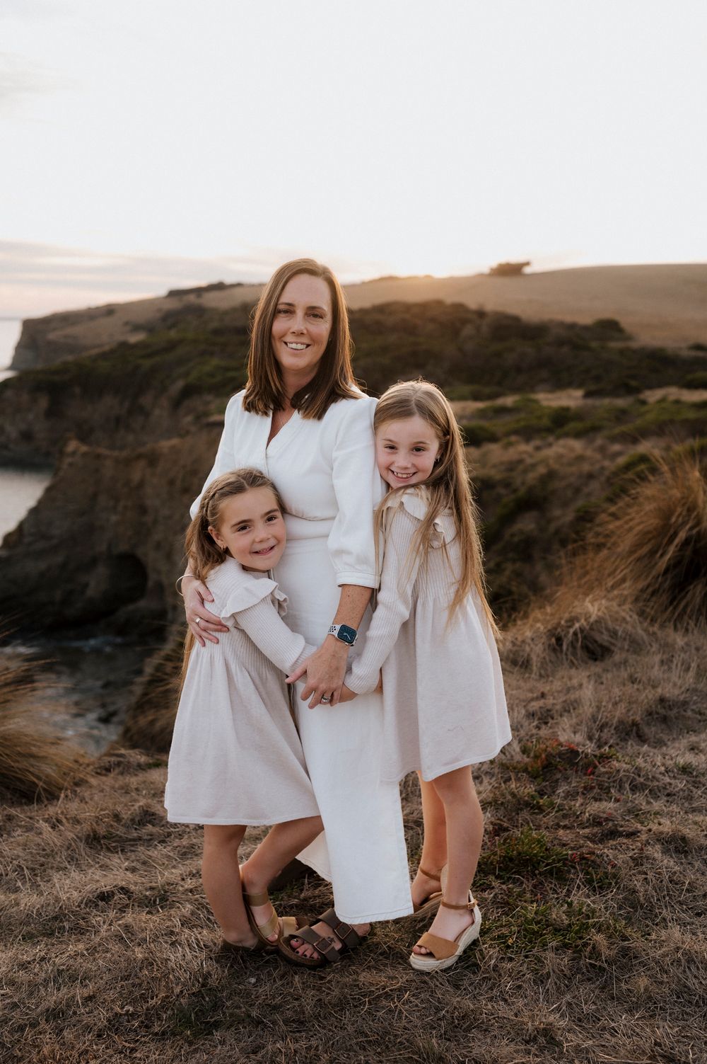 Beautiful coastal family portrait with everyone dressed in white against dramatic cliffs.