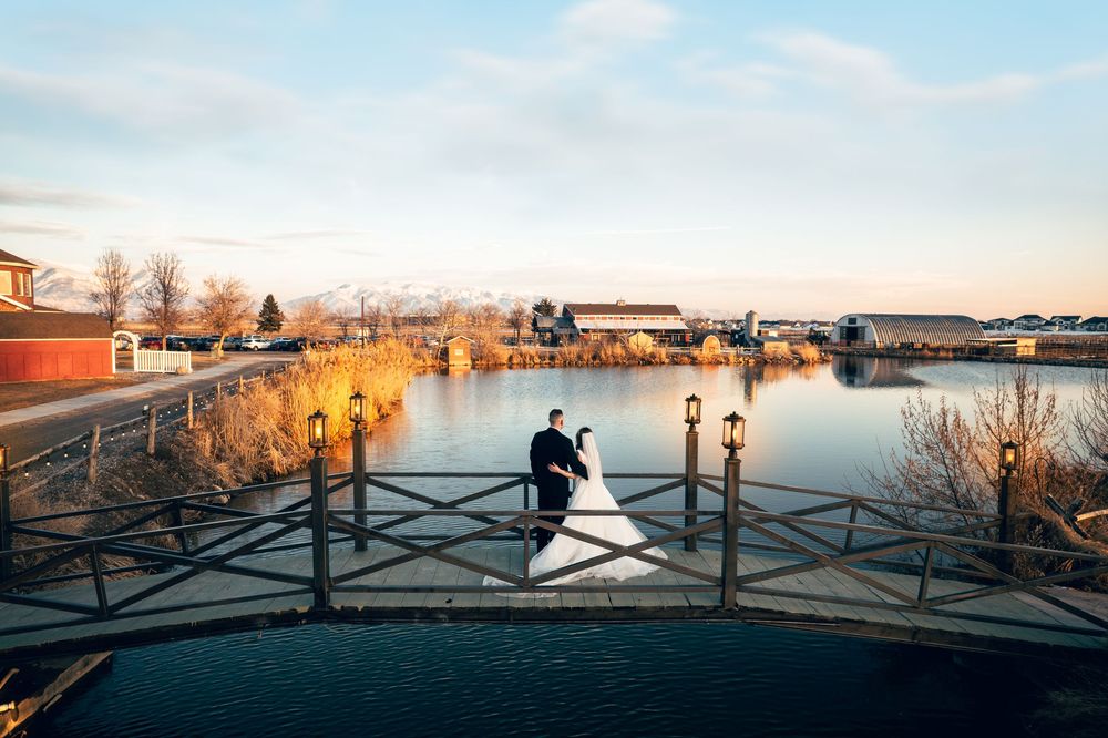 Bride and groom share romantic moment on bridge overlooking scenic lake at golden hour sunset.