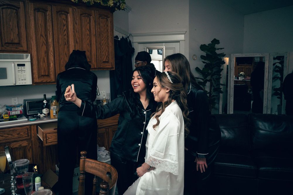 Bride taking a selfie with bridesmaids in pajamas during wedding morning preparations.
