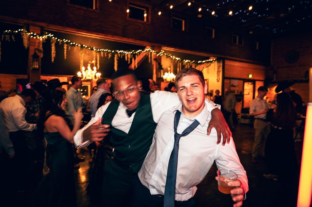 Two smiling groomsmen posing together at a warmly lit wedding reception.