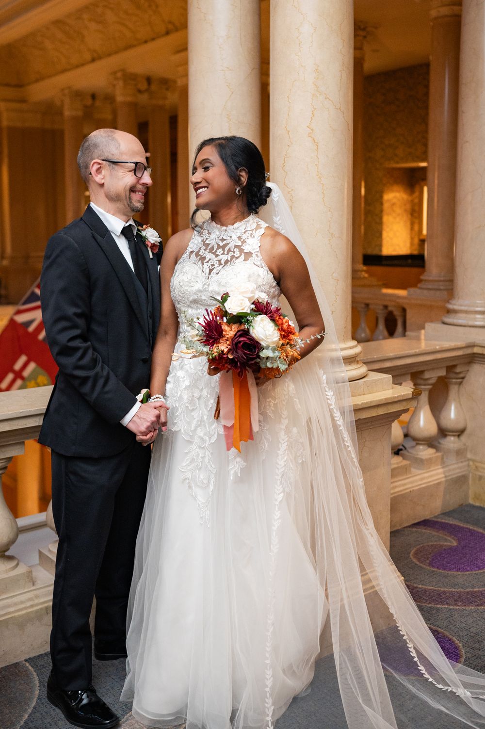 A happy couple shares a joyful moment on their wedding day, with the bride in a stunning lace gown holding a fall bouquet.