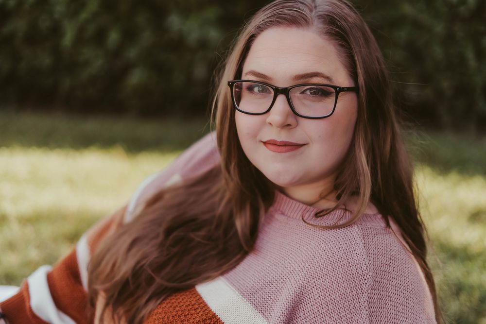 Teen girl with glasses and long auburn hair posing outdoors in colorful striped sweater.