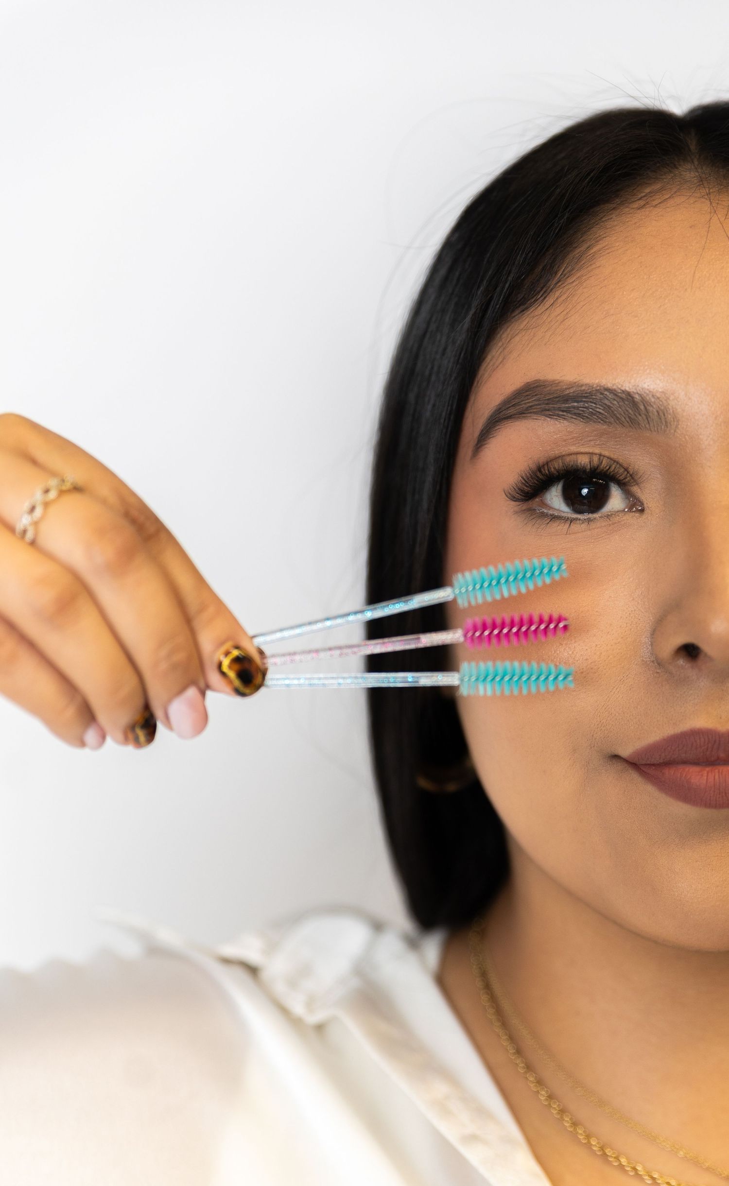 Hand holding colorful mascara wands against white background.