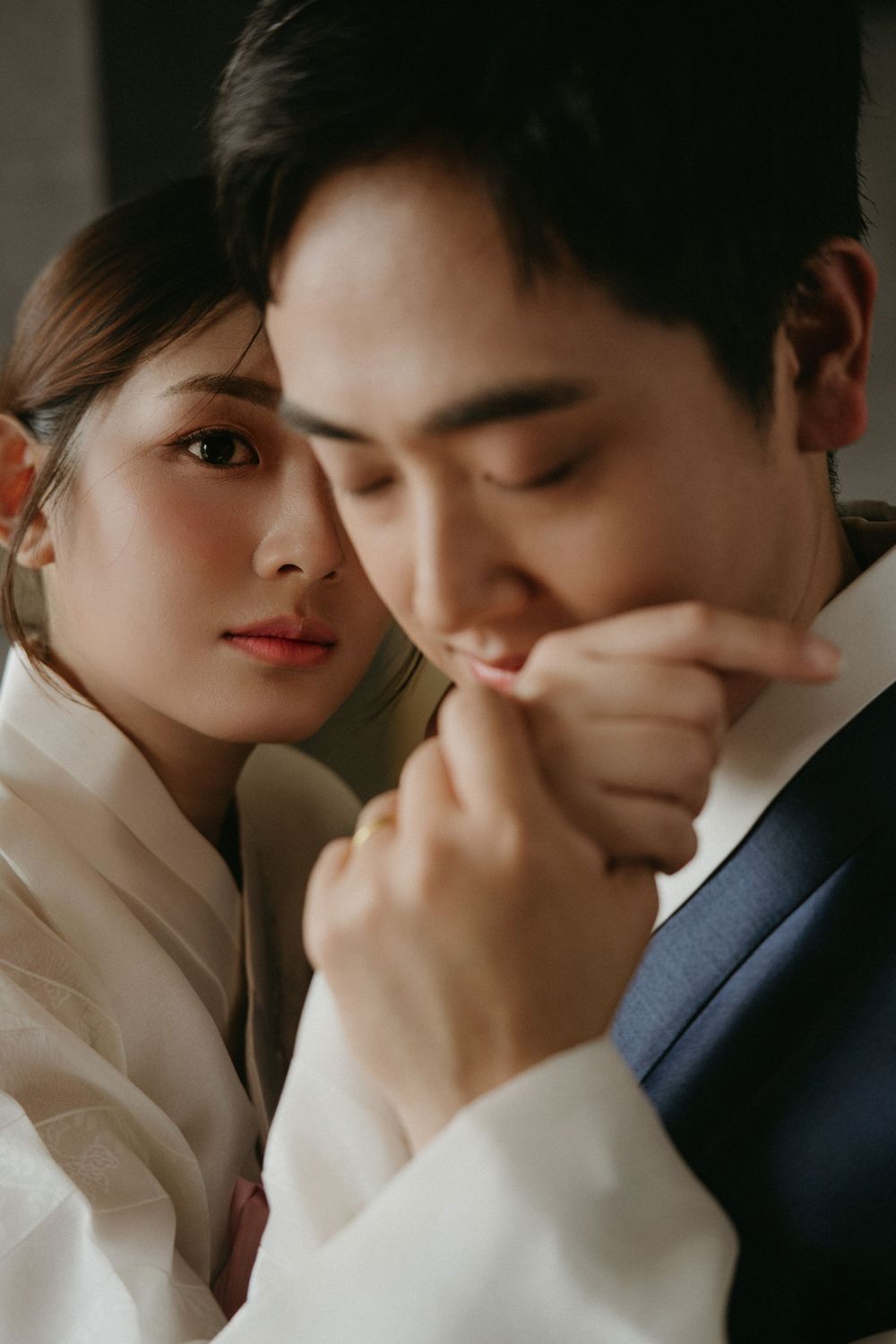 Romantic couple in intimate pose with person in navy suit gently holding hands of partner in white attire.