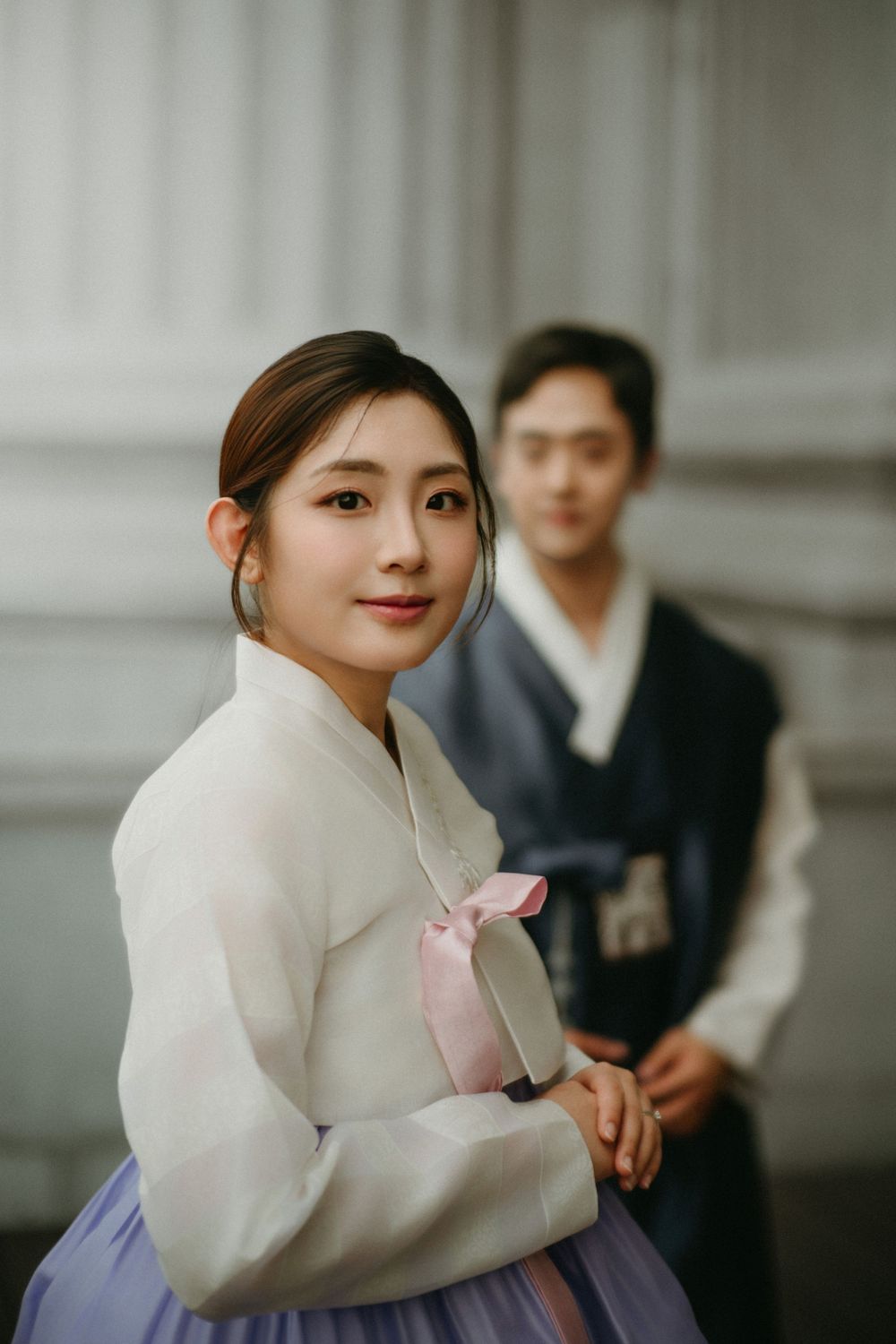 A couple wearing traditional Korean hanbok attire pose together against a neutral background.