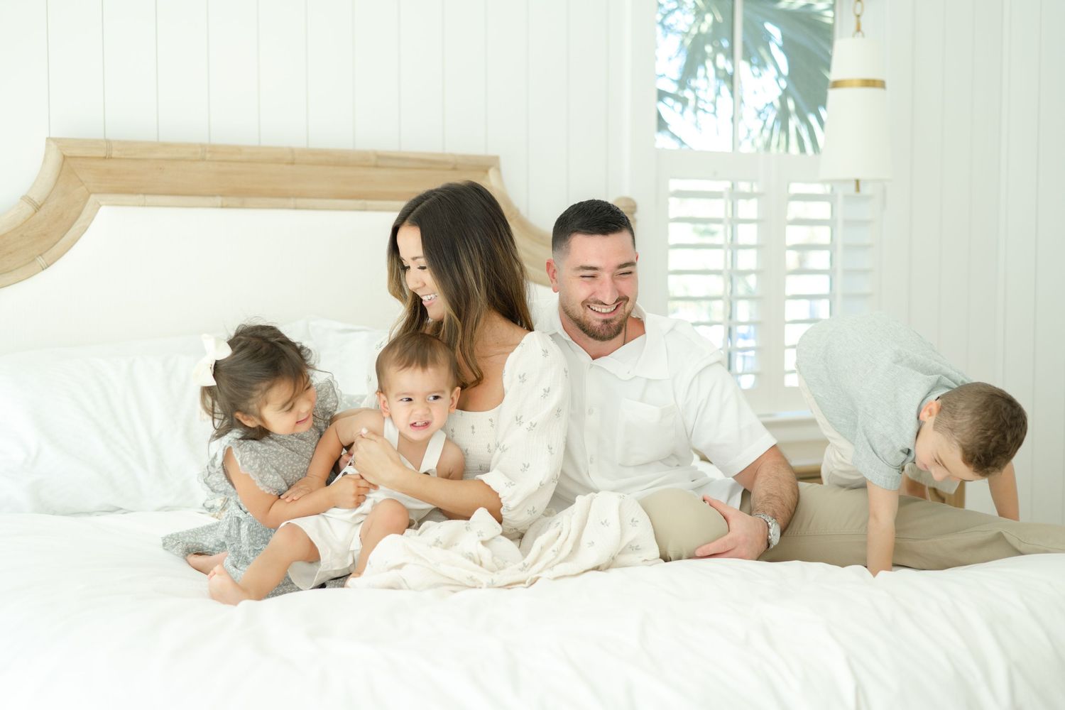 A loving family with three young children enjoys a playful moment together on a white bed.