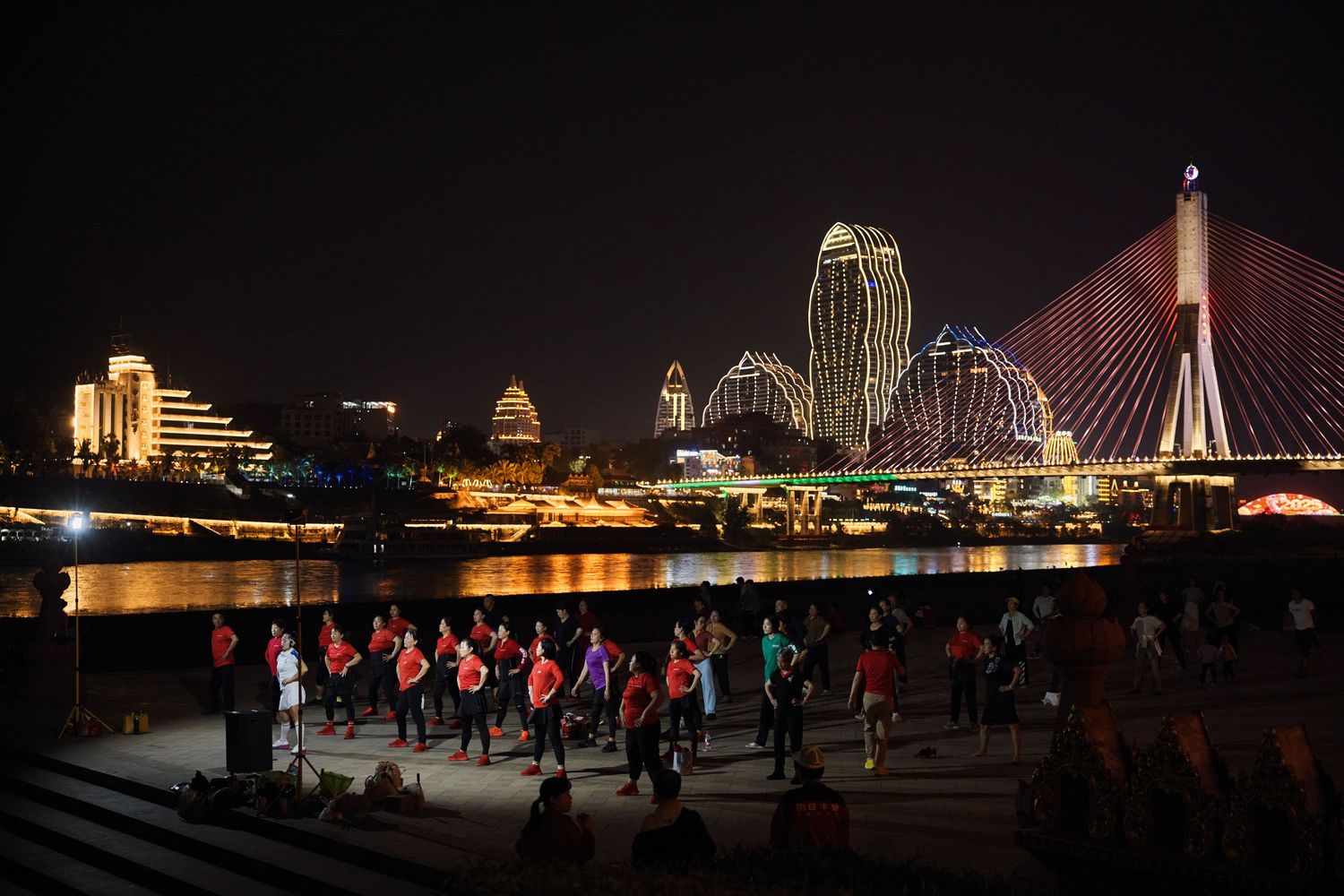 A group of runners exercising along the waterfront at night with illuminated bridges and Boston skyline visible in background.