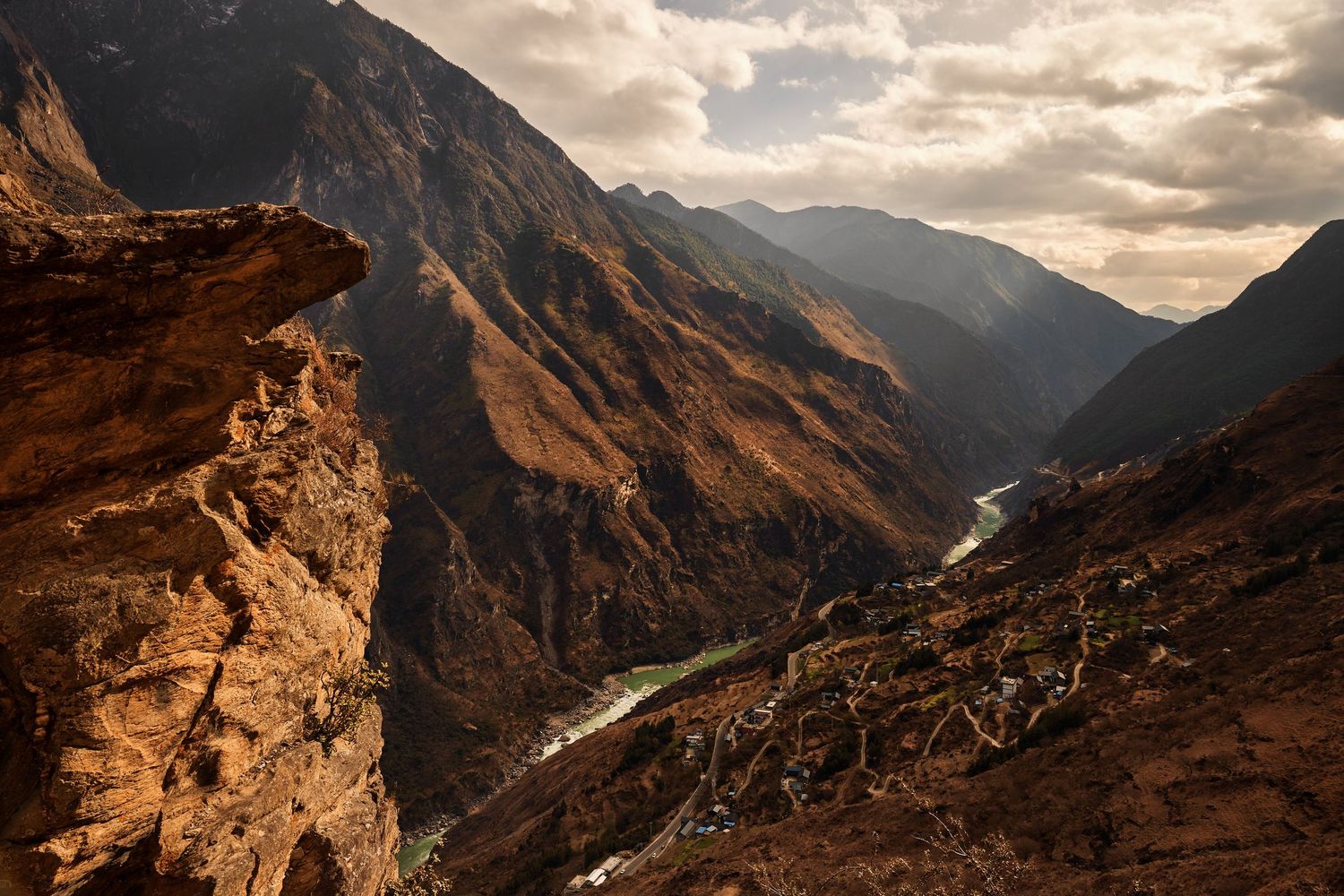 Dramatic mountain gorge with steep rocky cliffs and winding river valley under cloudy sunset sky in remote wilderness.