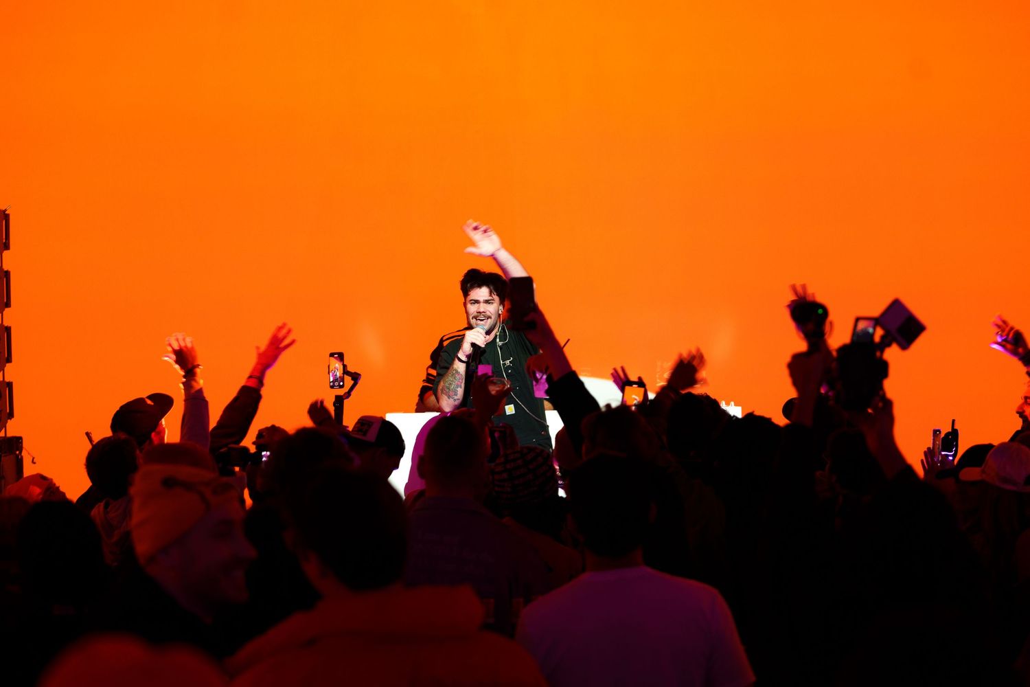 Silhouette of performer on stage against bright orange background with crowd cheering.