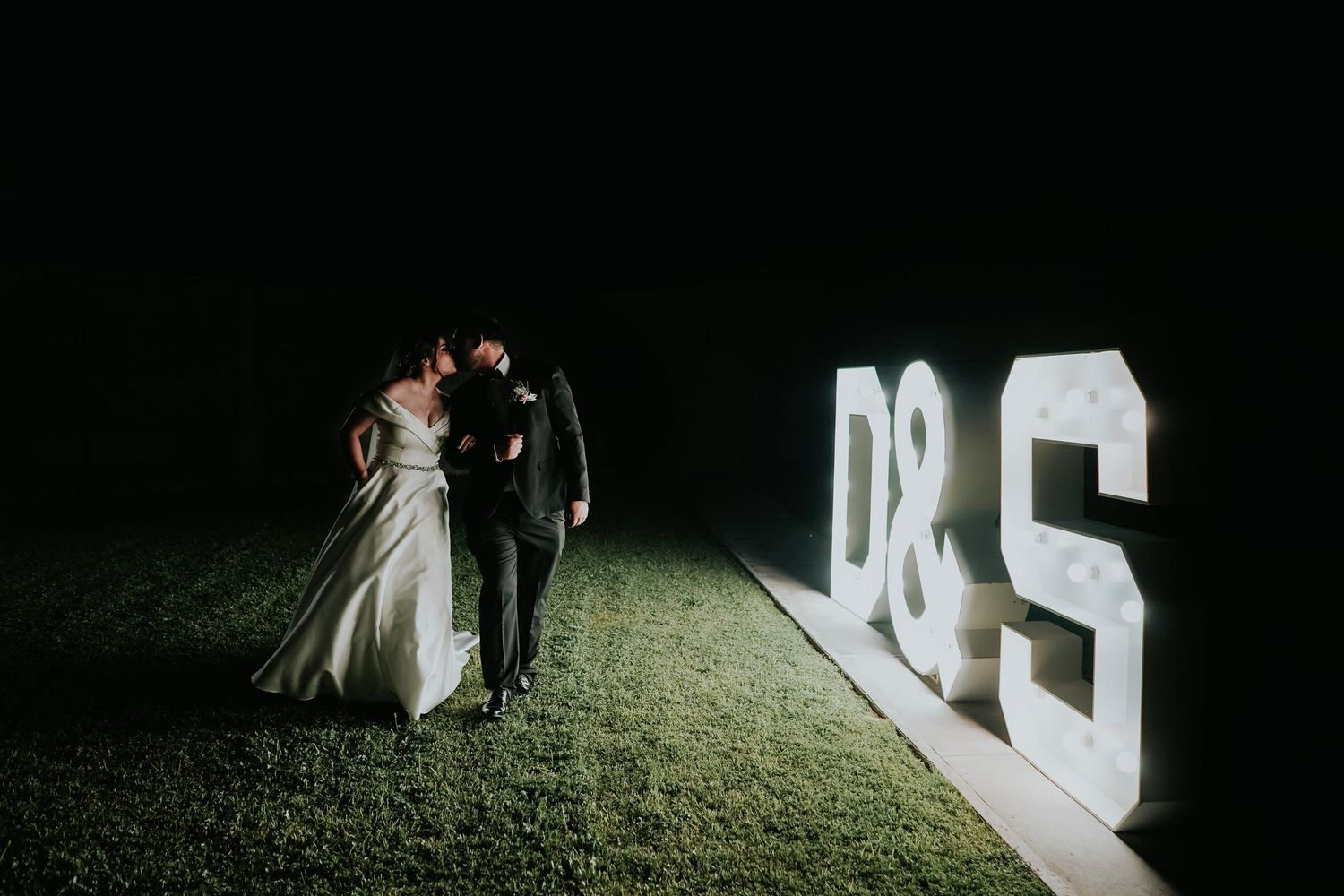 A wedding ceremony takes place inside a rustic stone archway with stained glass windows and floral decorations.