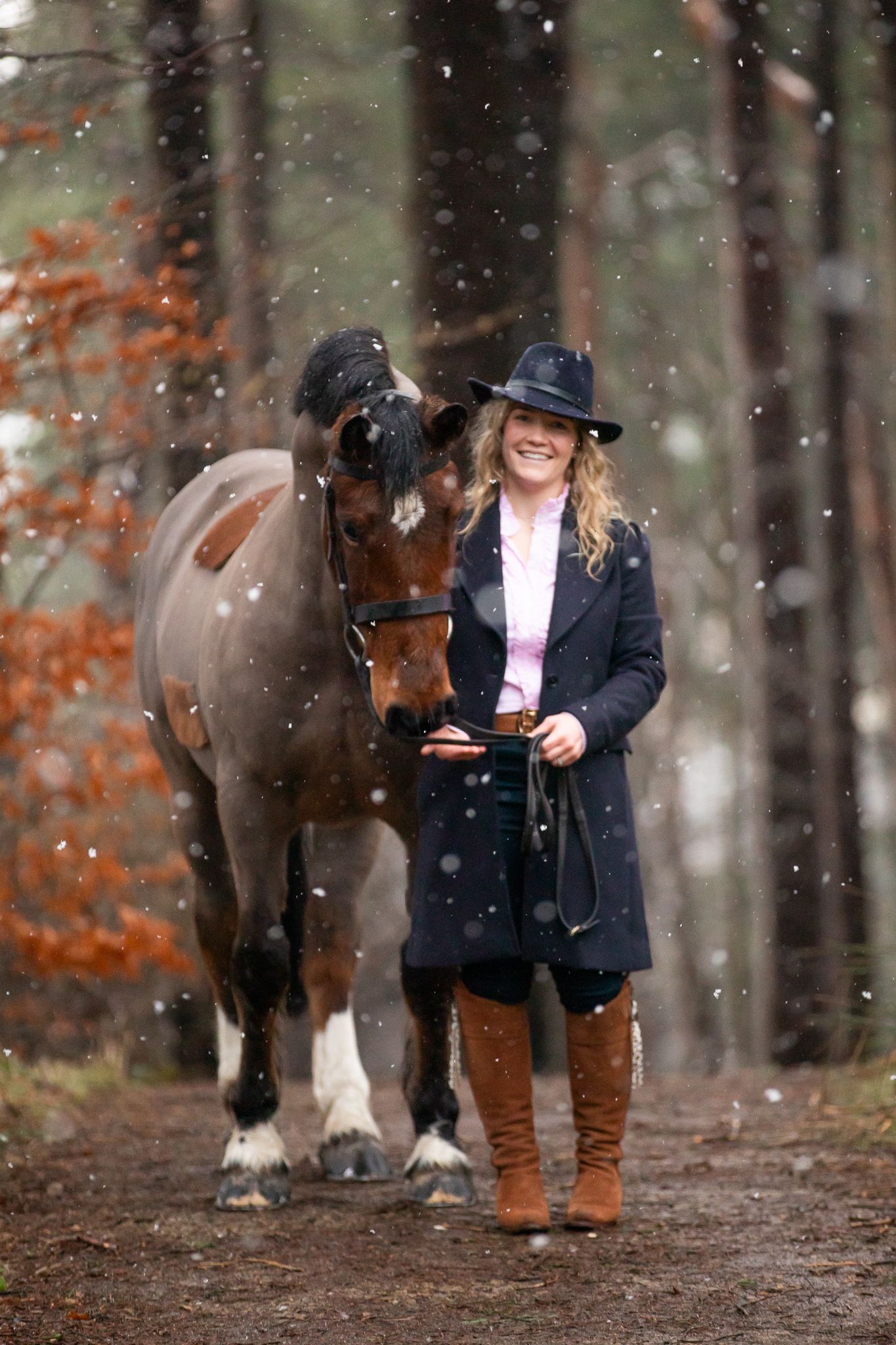 A beautiful white horse stands with its handler in brown winter attire on a hillside with dried vegetation.