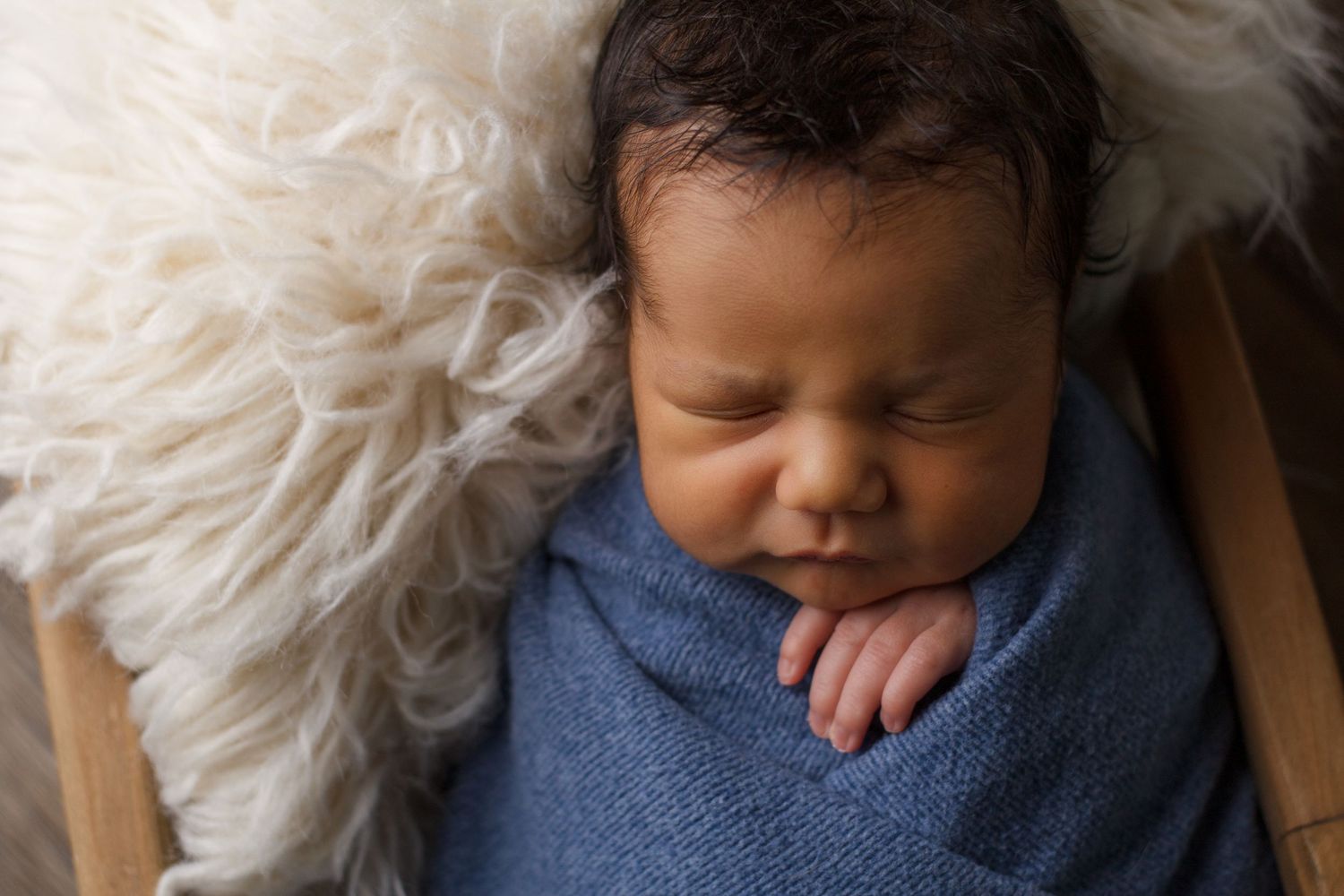 Newborn baby boy wrapped in blue laying inside n a wooden cage