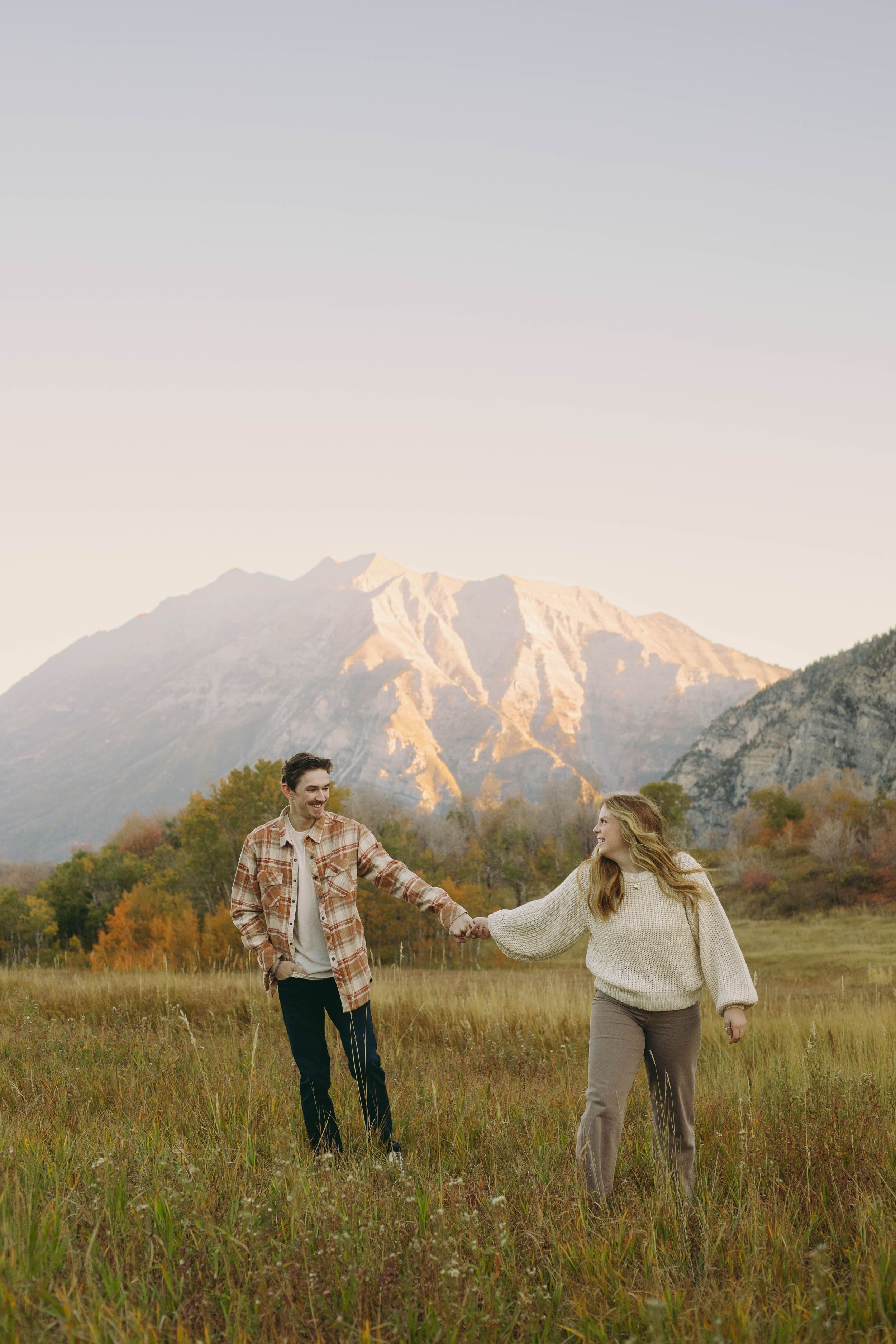 A playful couple holding hands in a mountain meadow during autumn in Provo, Utah.