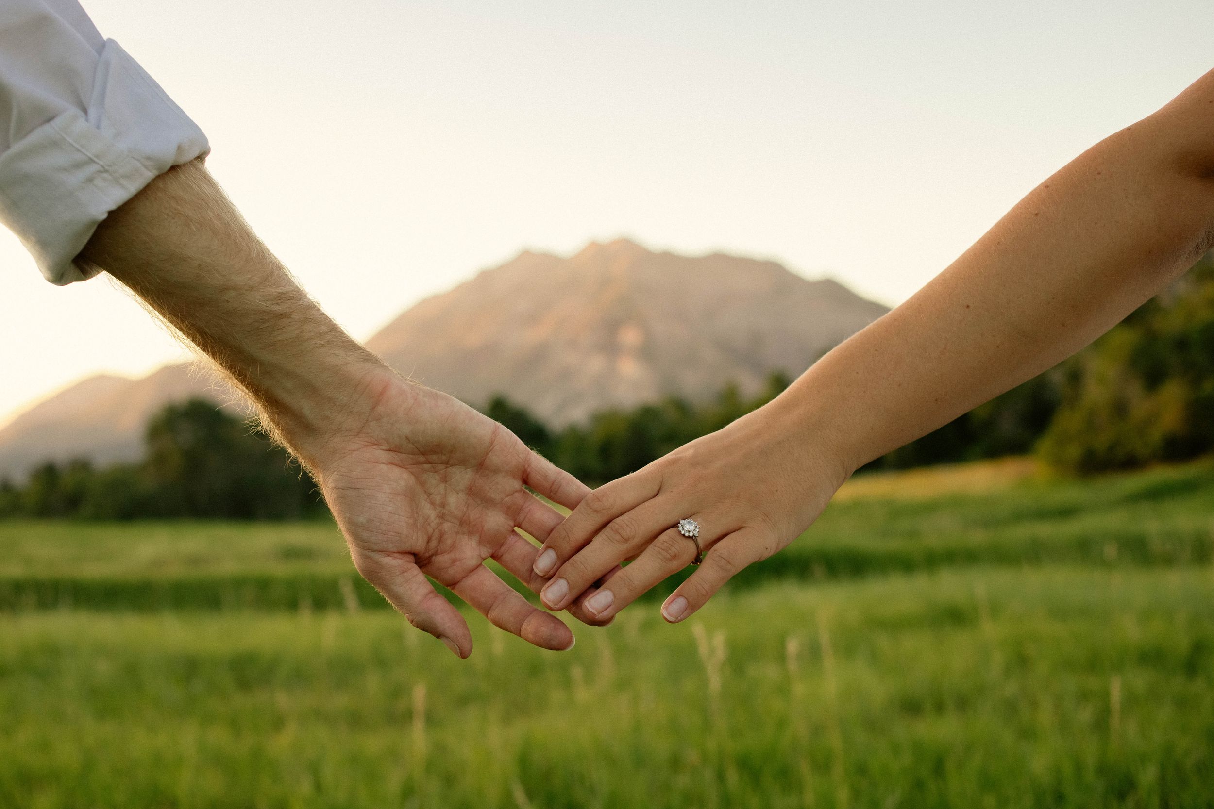 Two hands join together against a backdrop of mountains and grass at sunset in Provo, Utah.