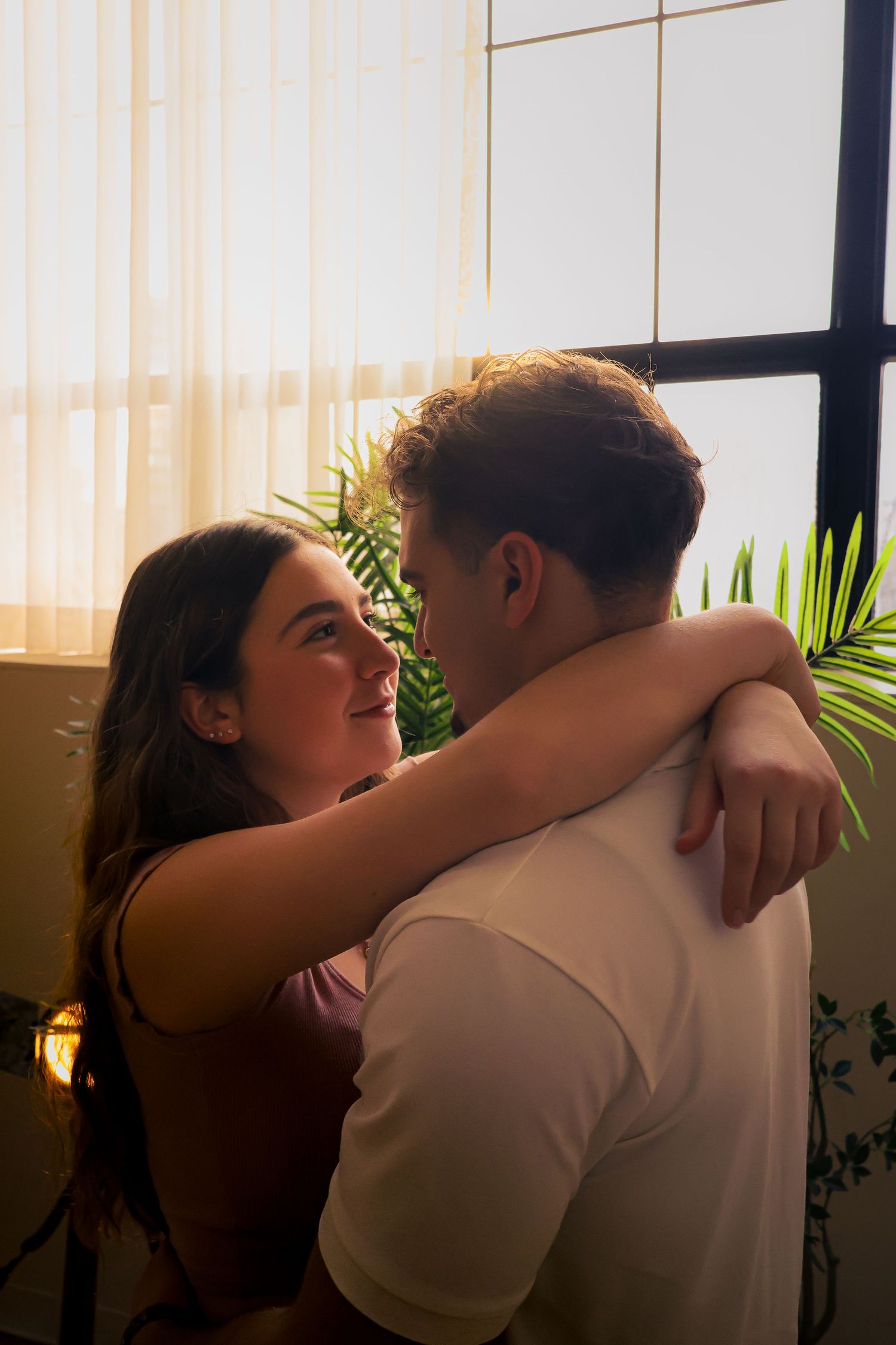 Couple embracing in front of a window, gazing into each other's eyes.
