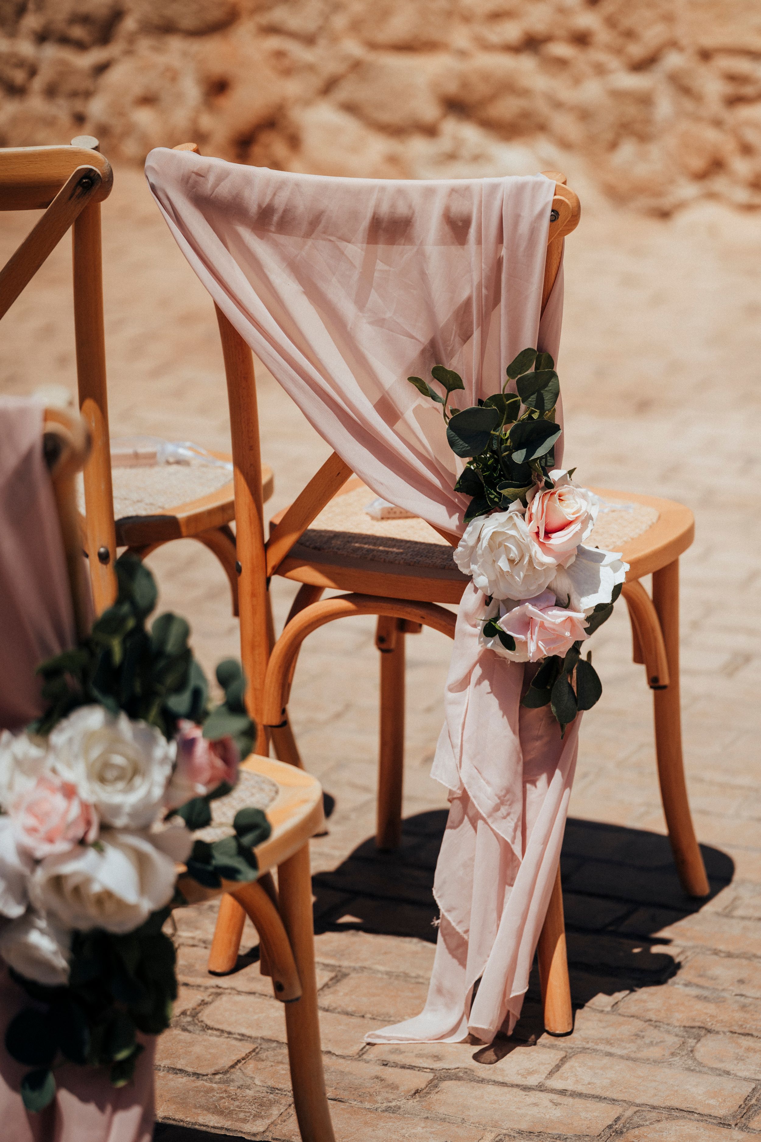 Close-up view of wooden ceremony chairs decorated with delicate pink fabric and white floral accents.