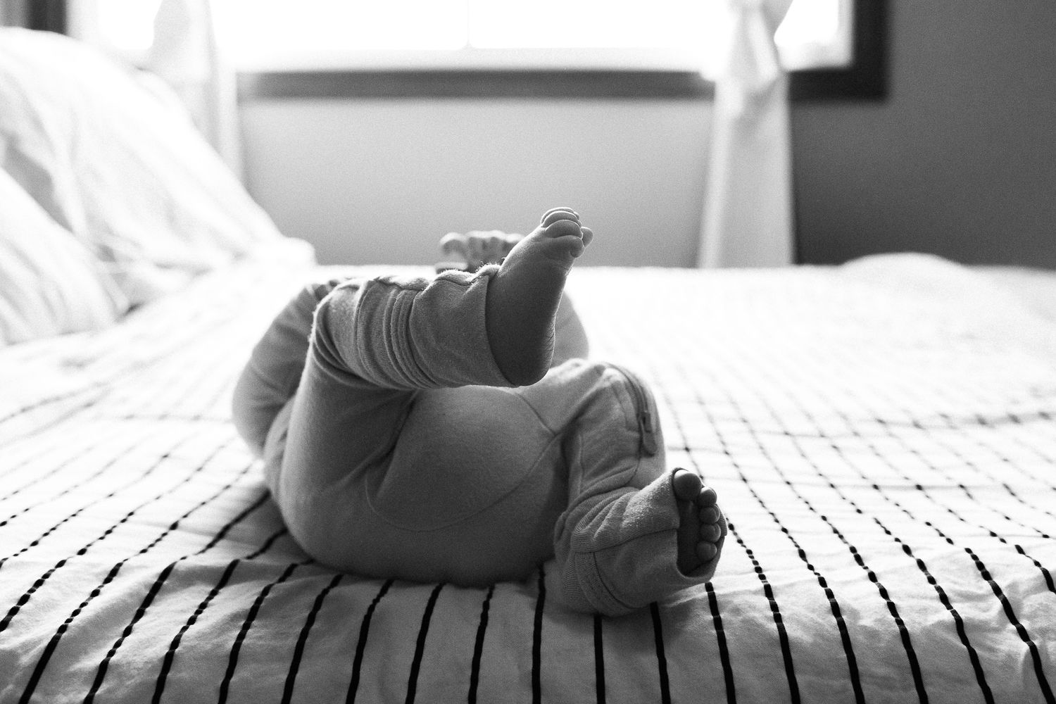 Small baby feet in monochrome lying on textured bedding in natural window light.