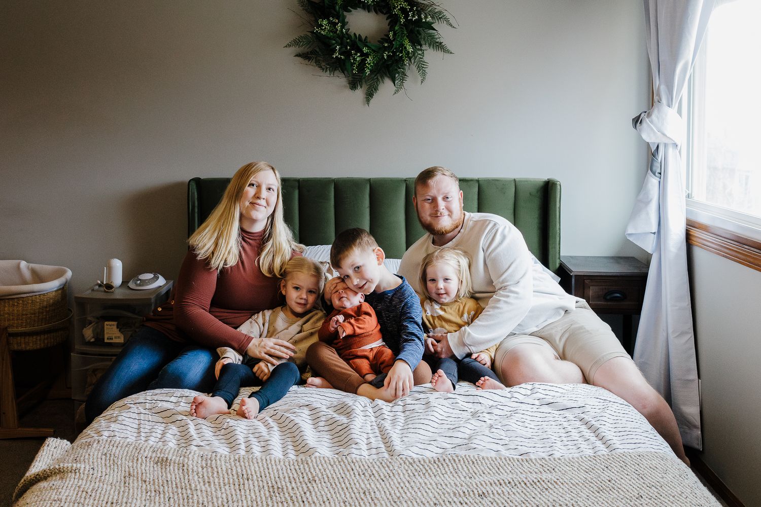 A cozy family moment on a bed with a green tufted headboard and holiday wreath on the wall.