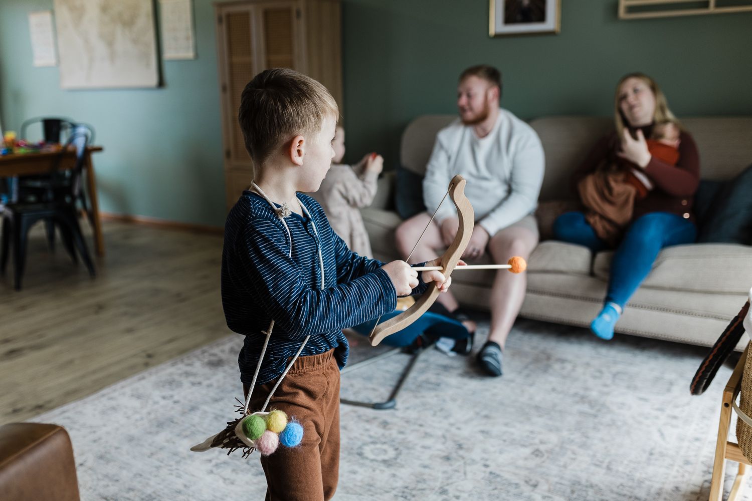 Child in denim plays with Easter eggs on carpet while others relax on living room couch.