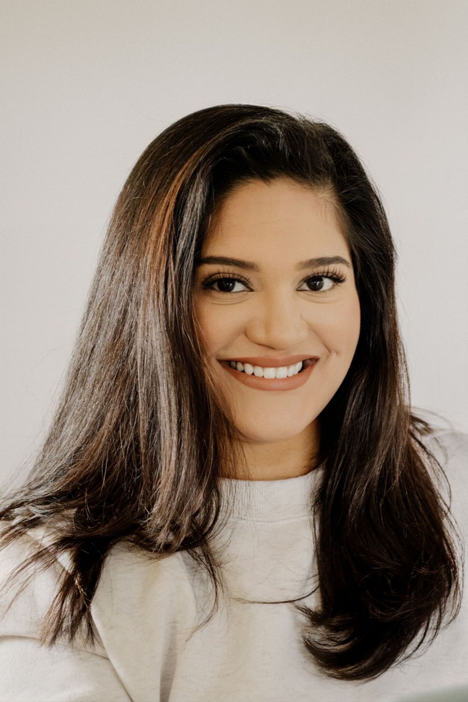 Young woman with long dark hair smiling warmly at camera against a clean white background.
