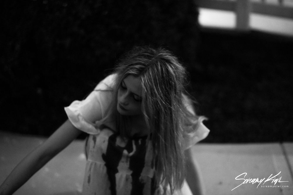 A haunting black and white photo shows a person in a blood-stained dress leaning forward.