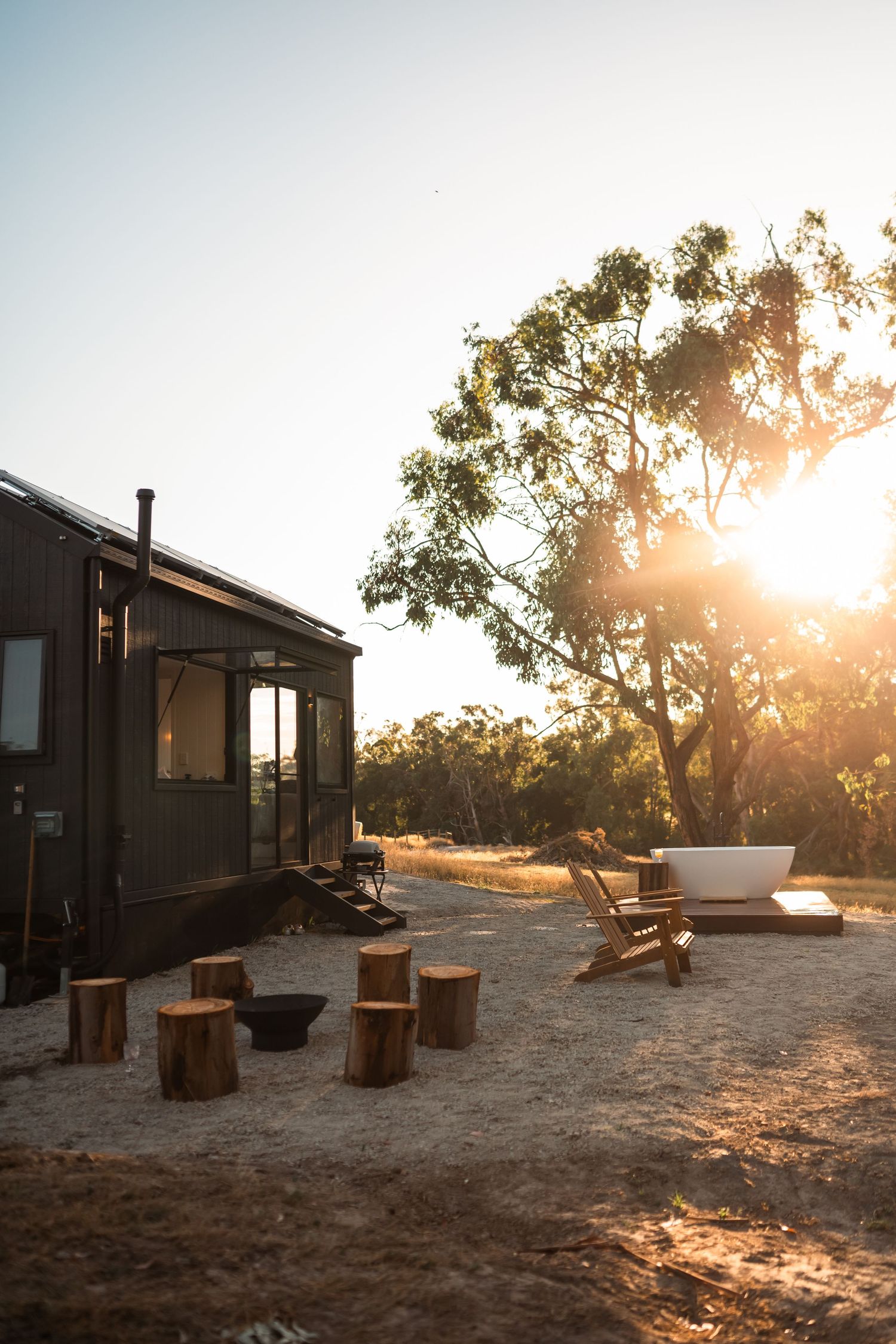 Rustic tiny house accommodation with outdoor seating among eucalyptus trees at sunset"