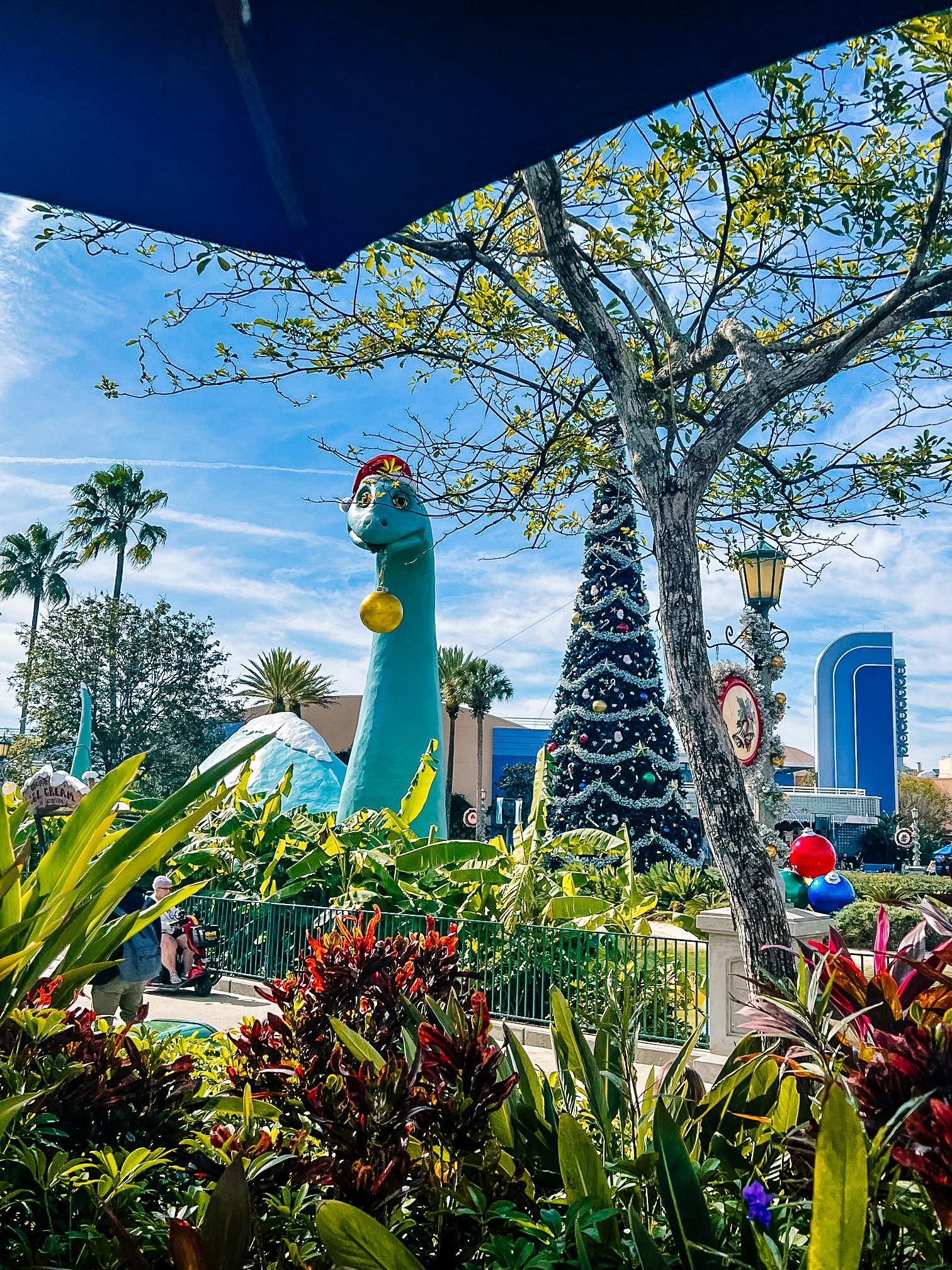 Tropical garden with tall palm trees and decorative dinosaur figures against blue sky.